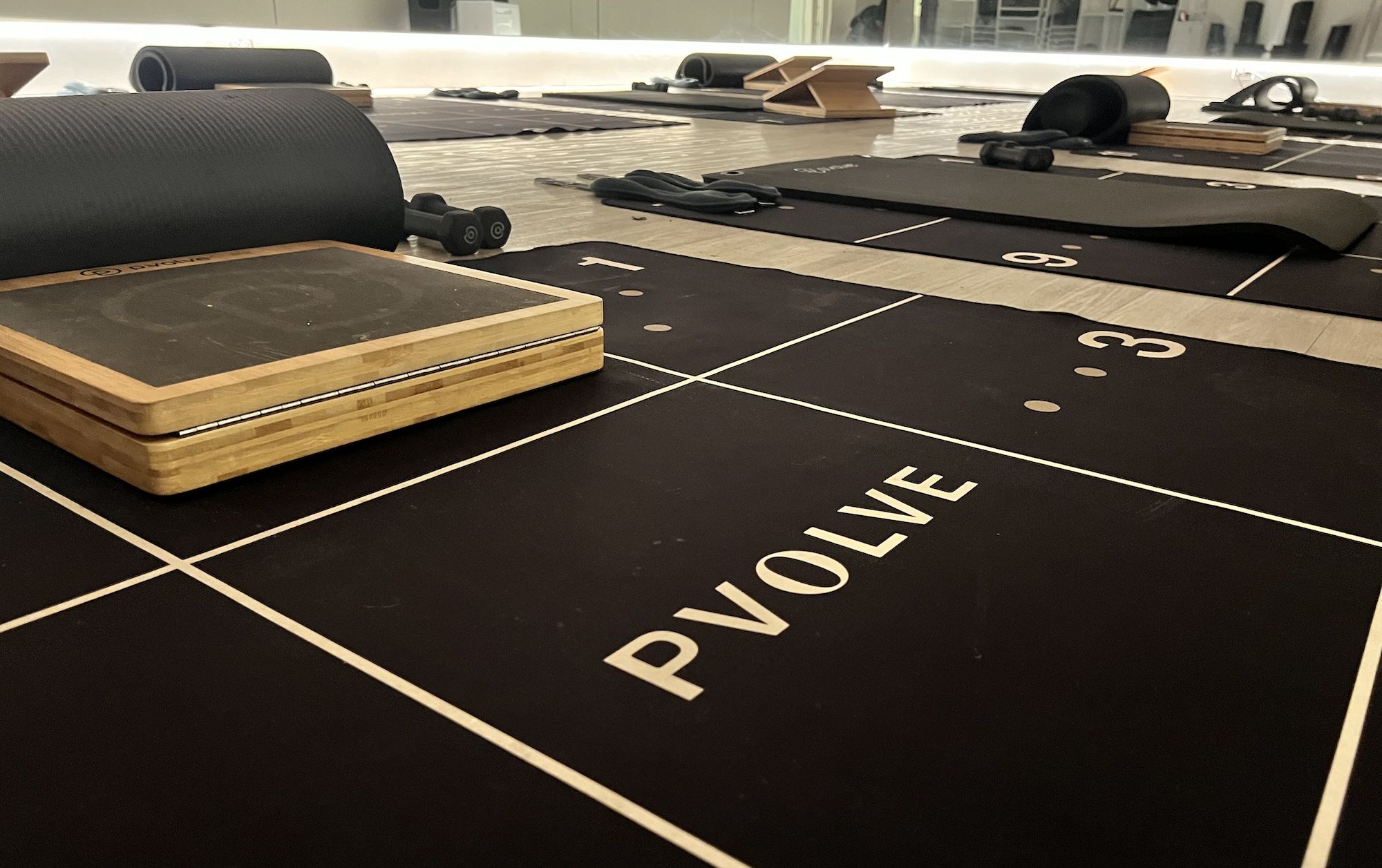 A close-up of a black mat with small wooden step, yoga mat and hand weights.