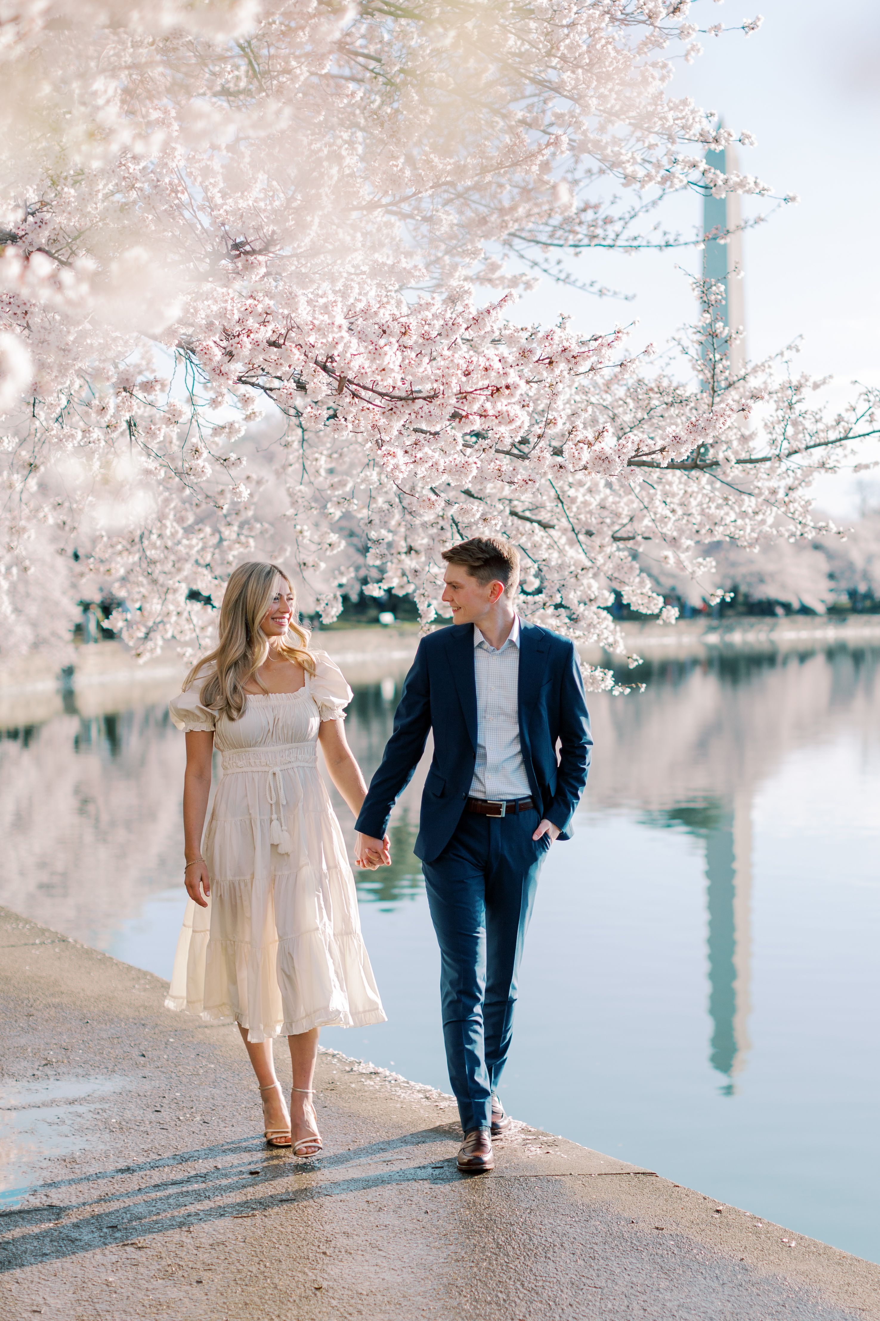 A couple poses in front of cherry blossoms with the monument in the background.