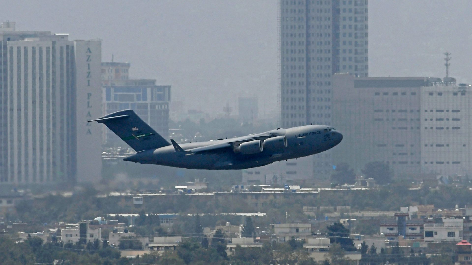 Photo of a U.S. Air Force aircraft flying against the backdrop of the Kabul skyline