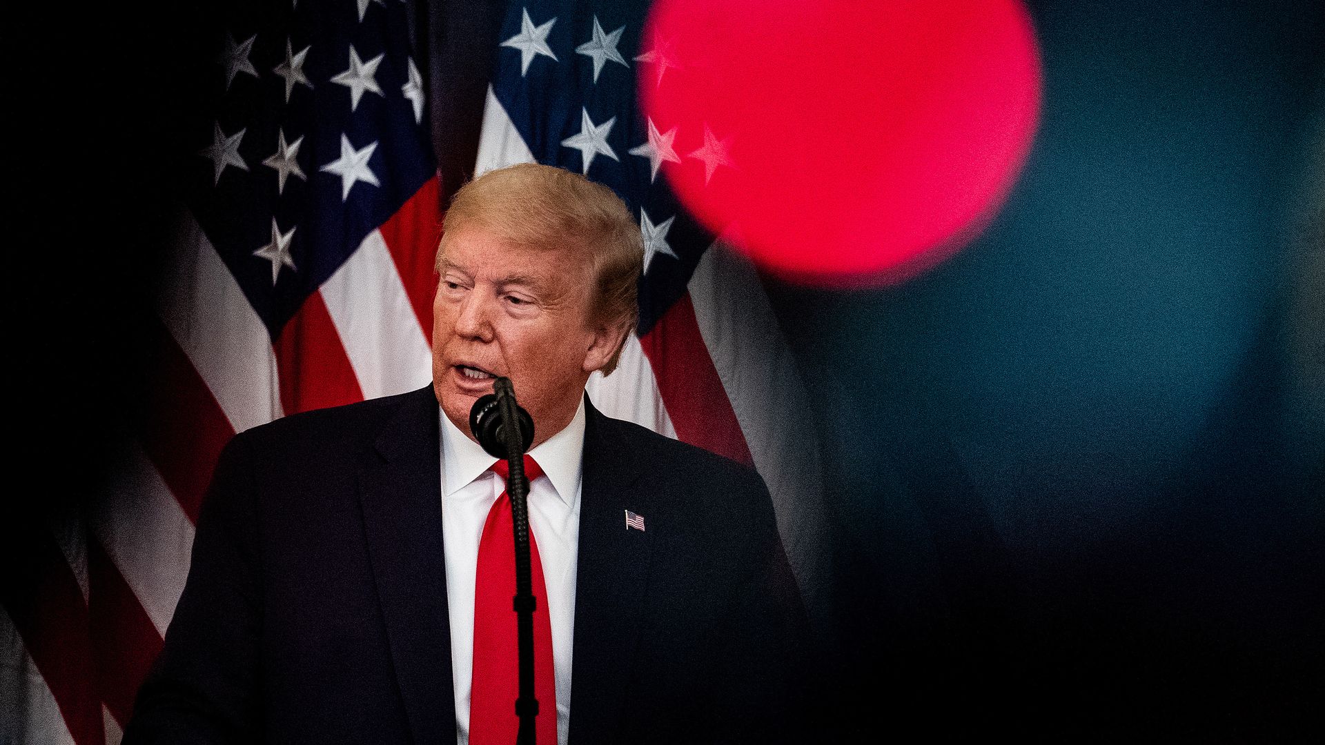 In this image, Trump stands in front of a flag
