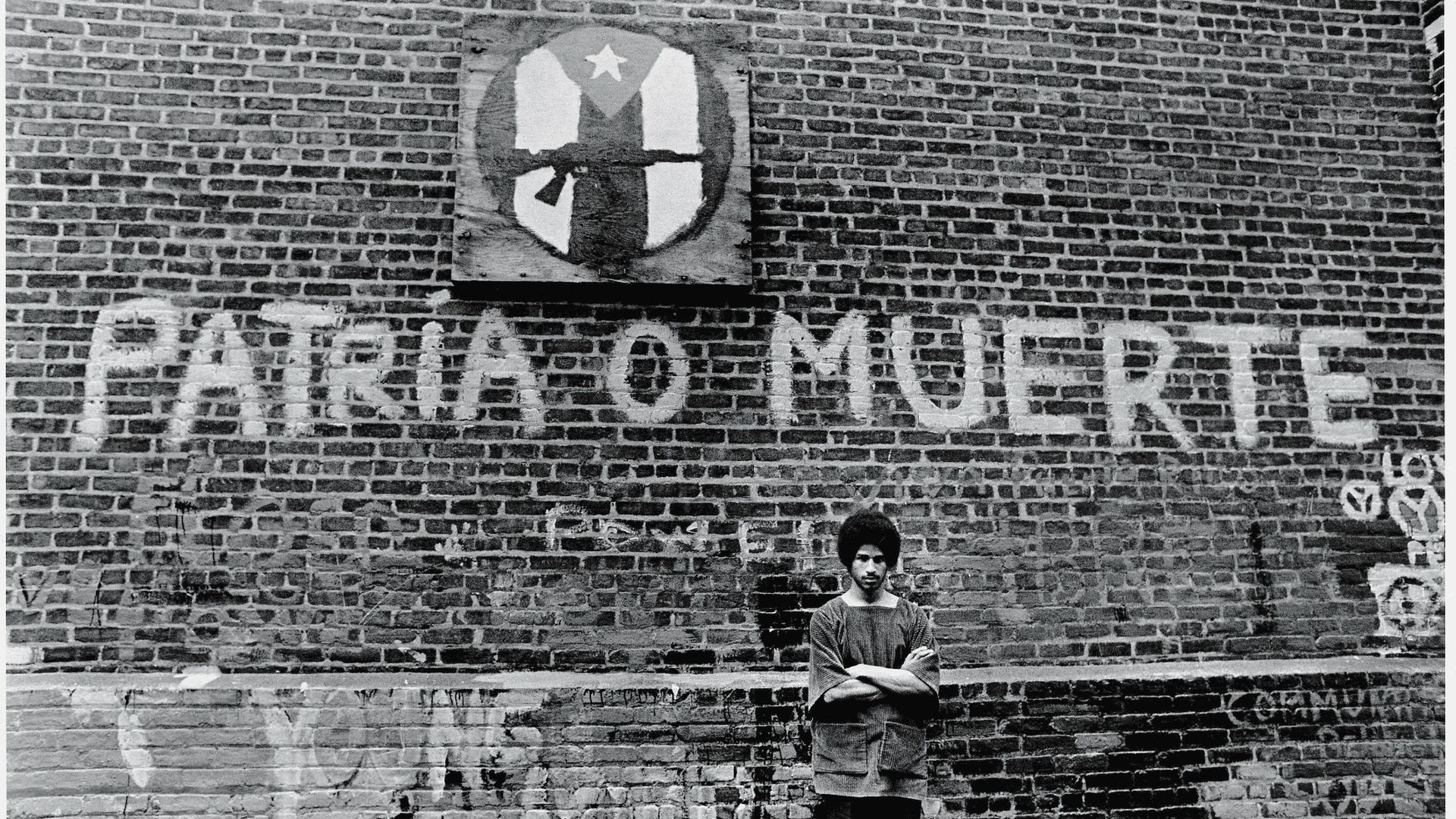 Portrait of American political and social activist Felipe Luciano and members of the Young Lords Organization (of which Luciano was a co-founder) as he stands with his arms crossed in front of a brick wall in Newark, New Jersey, July 23, 1970.