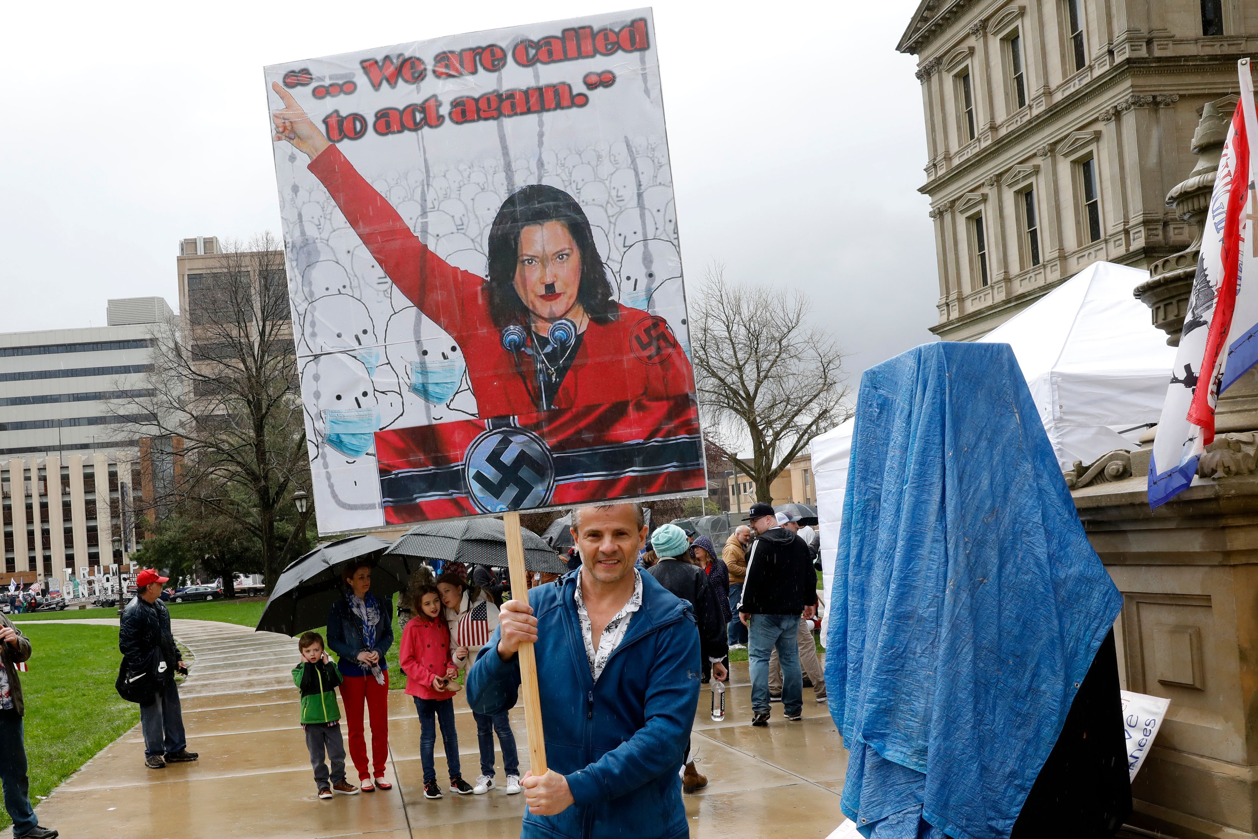 A protestor with a sign that has Michigan Gov. Gretchen Whittmer depicted as Adolph Hitler