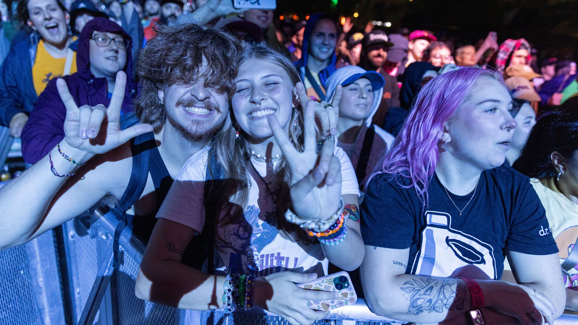 Photo of music fans at an outdoor festival making peace signs with their hands as they pose for the camera. 