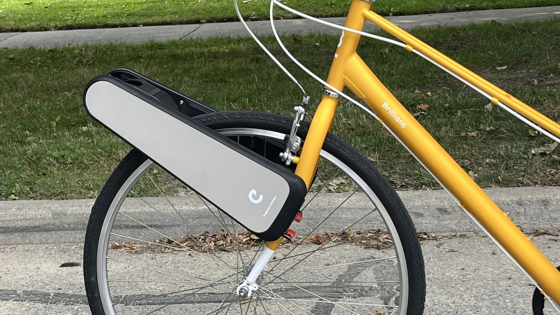 A gray triangular Clip device straddles the front wheel and fork of a yellow bicycle.