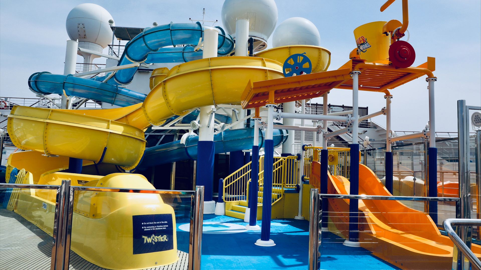 Image shows yellow, blue and orange waterslides on a cruise ship deck.