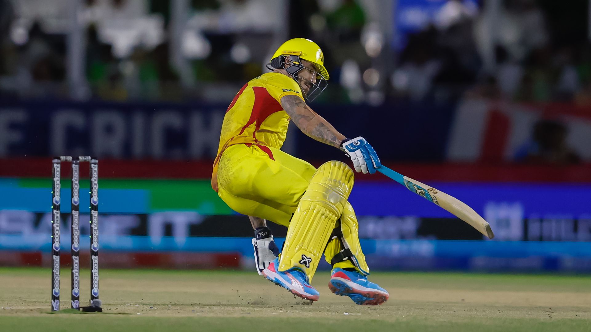 An athlete wearing yellow and holding a bat leans backward on a field