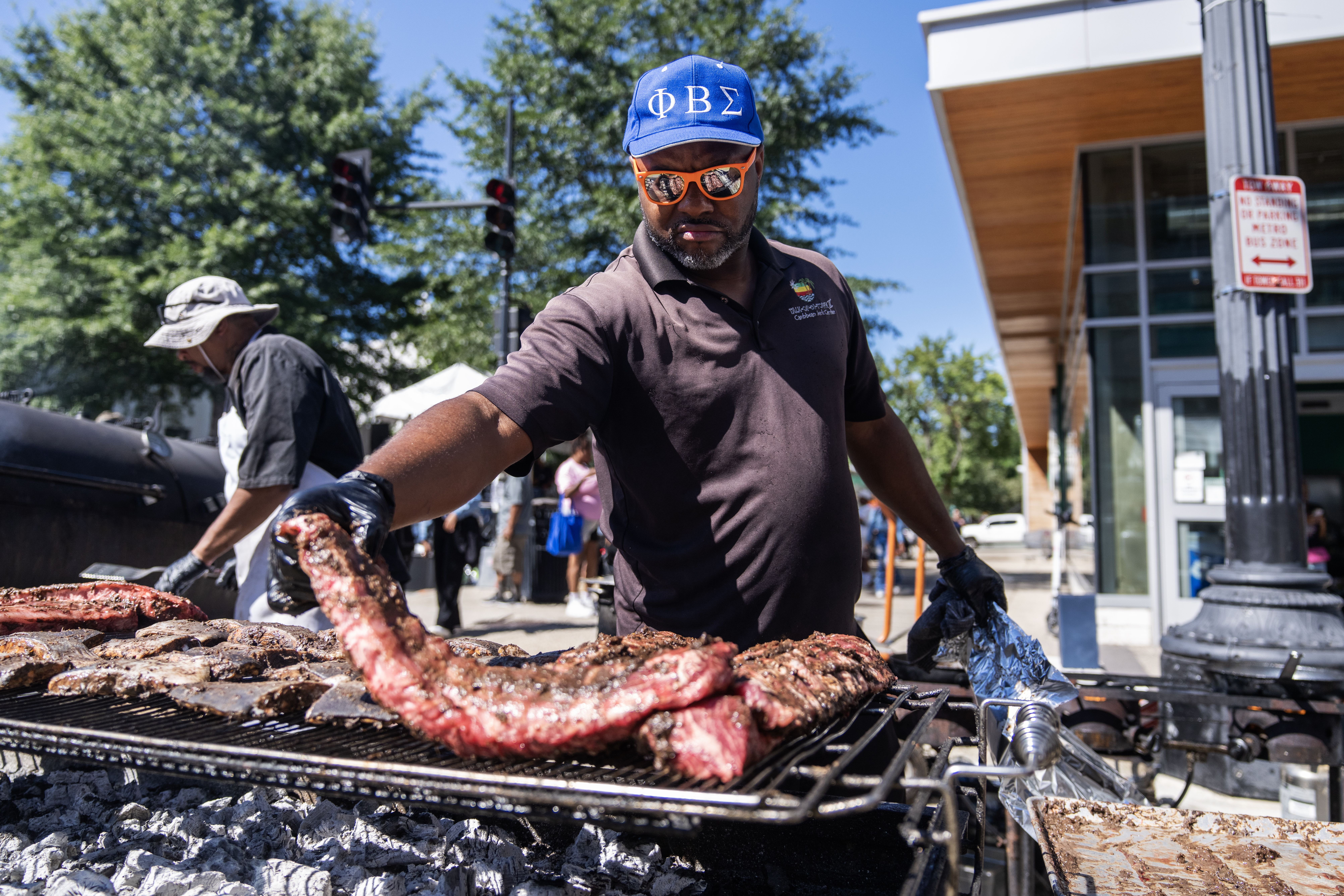 A man in a hat and sunglasses lays ribs on a grill 