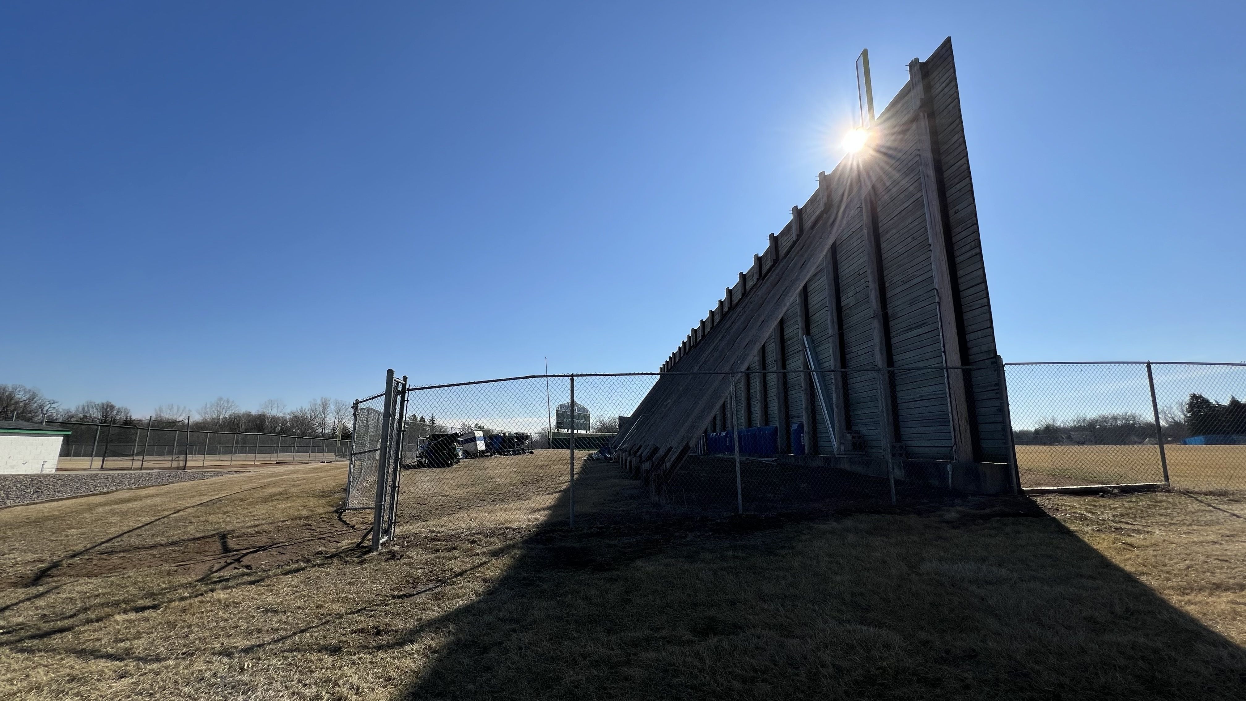 The rear of a tall outfield fence with the silhouette of sunlight shining behind it