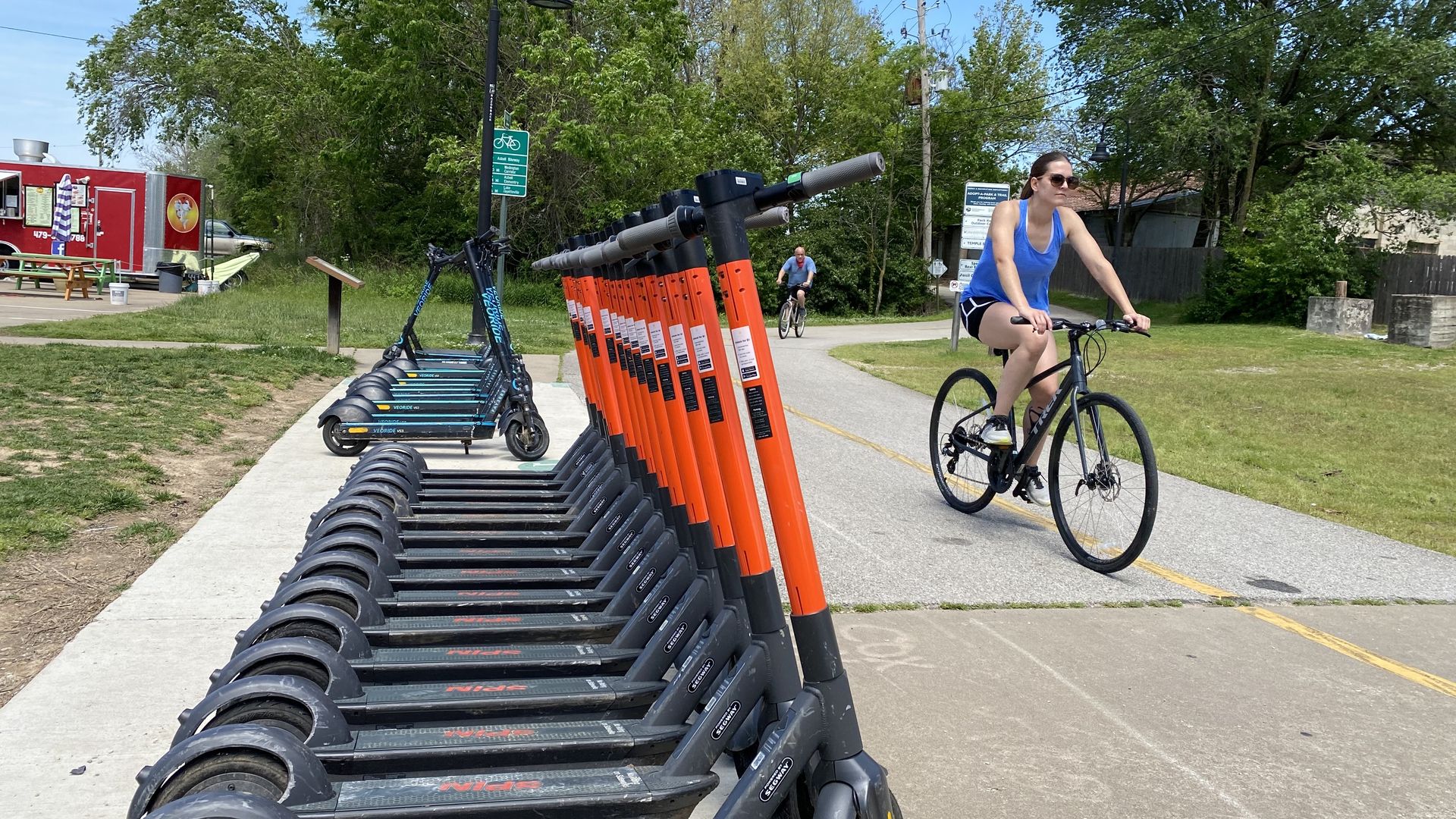 A woman on a bike rides past e-scooters on the Razorback Greenway. 