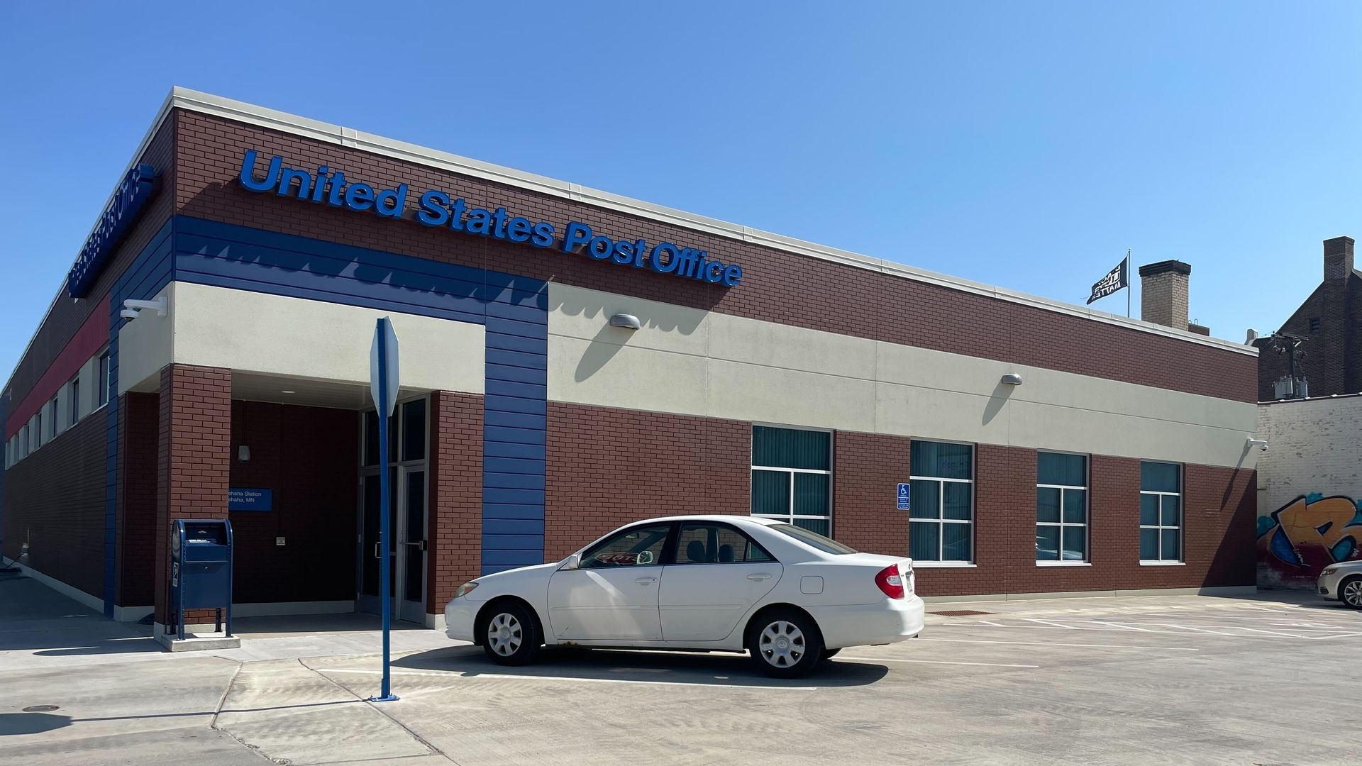 brick building with blue united states post office lettering and white car out front