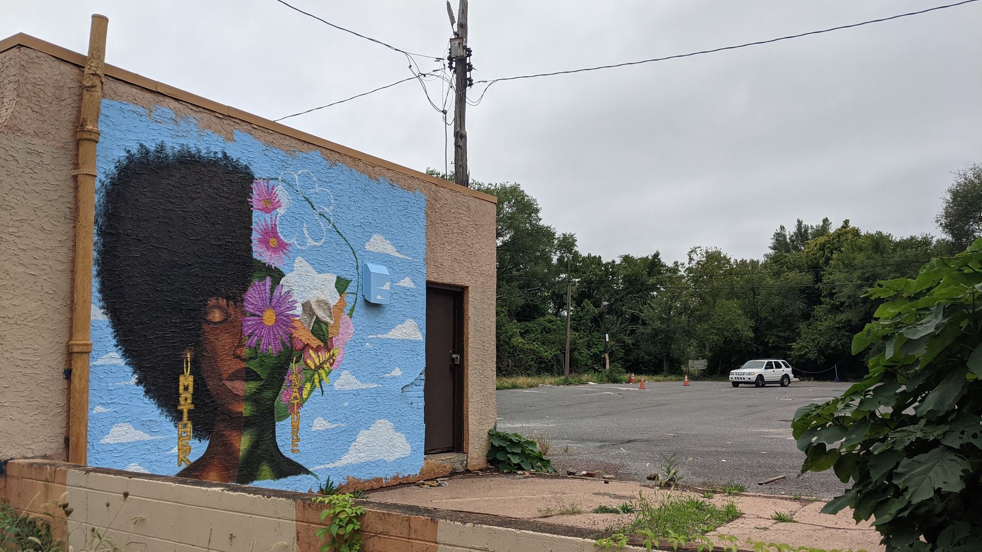 A mural of an African American woman wearing earrings that read "Mother" and "Nature" is painted on vacant one-story building at N 49th Street and Parkside Avenue in West Philadelphia.