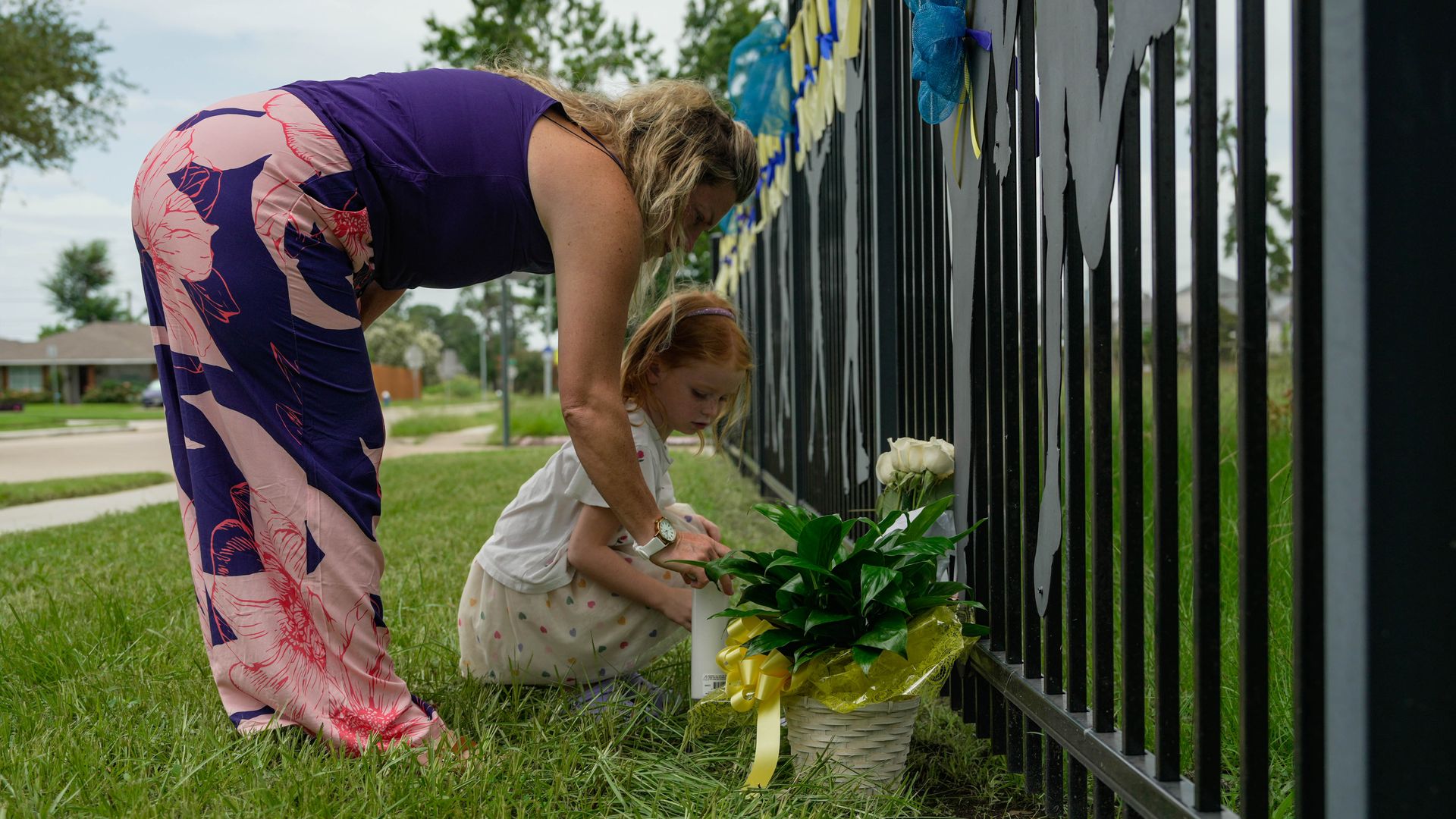 A woman and her daughter bring flowers and a candle to a fence memorial for flooding victims.