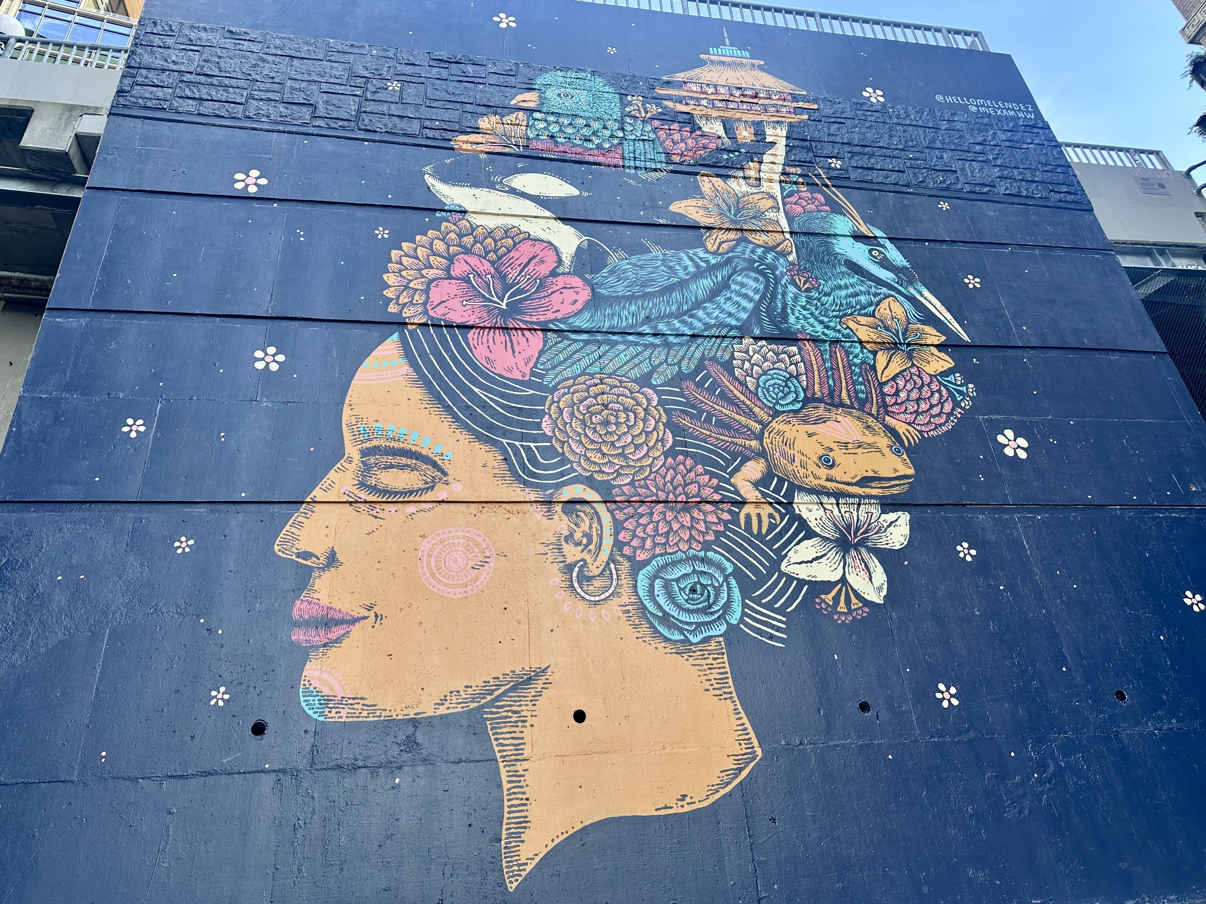 A photo of a mural of a woman's face in profile with a Space Needle among the decorative elements in her hair, along with flowers.
