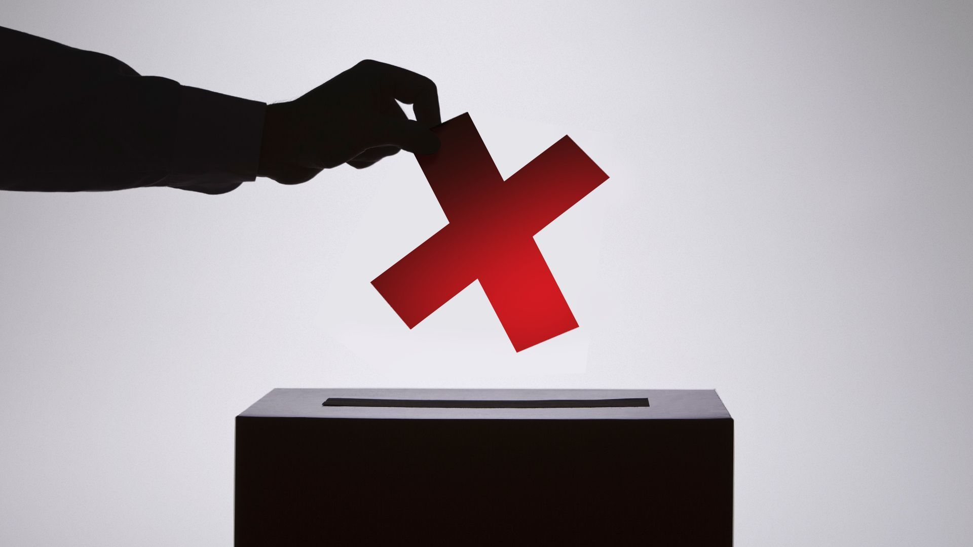 A silhouetted hand places a red X into a ballot box.