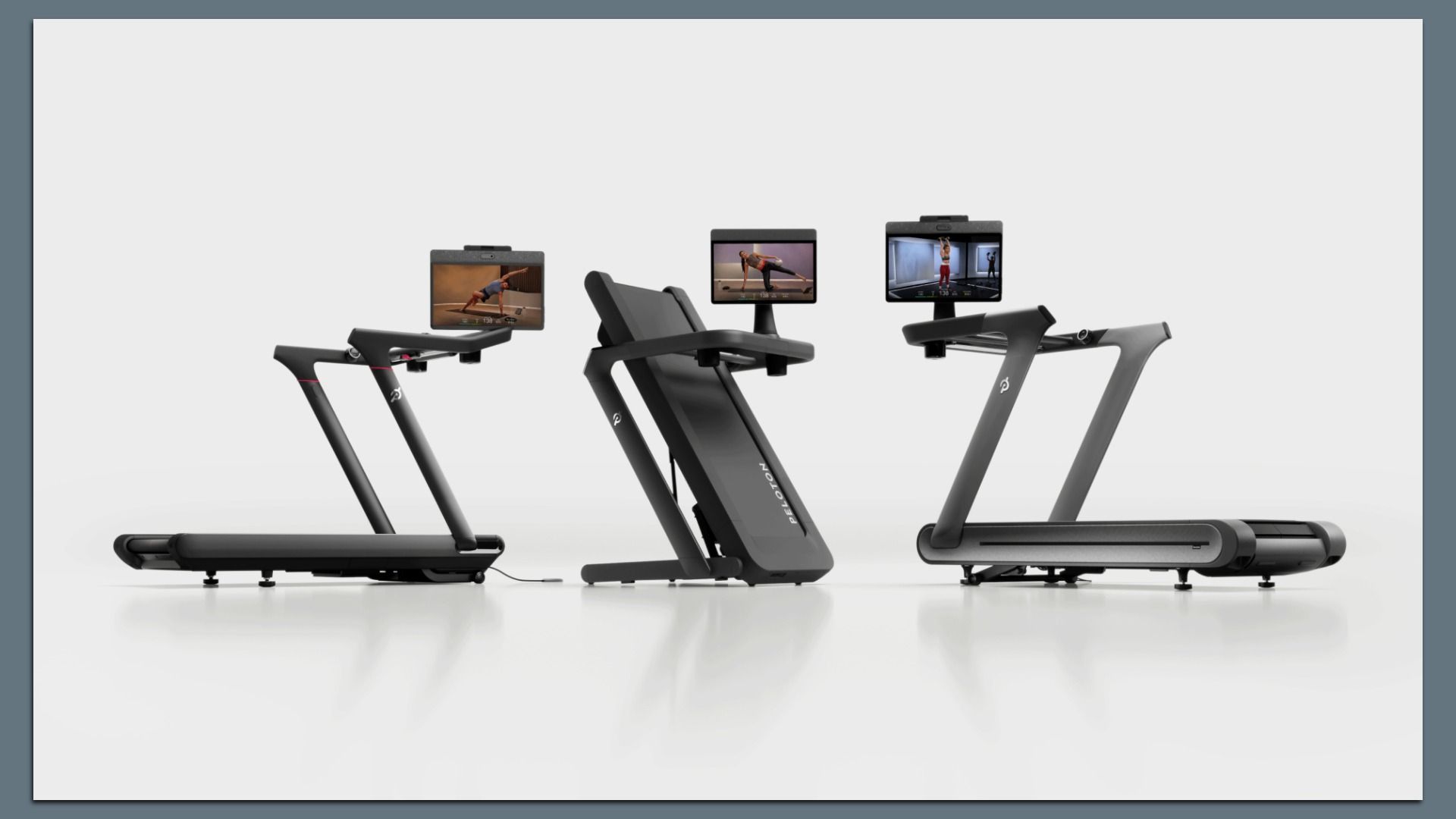 Three modern treadmills with small screens mounted on the handlebars displaying workout scenes; black and gray frames on a pale gray studio backdrop.