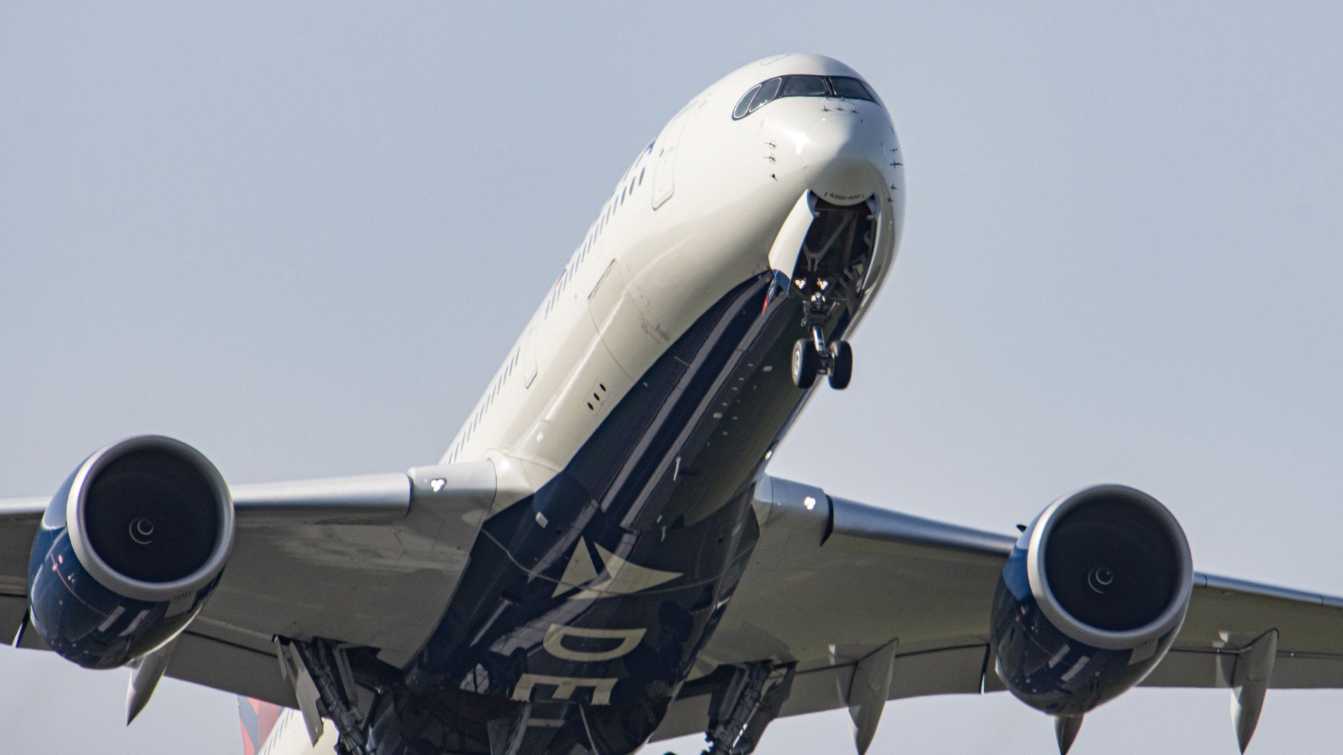 Close-up of a white and blue commercial airplane with landing gear extended, flying against a clear sky.