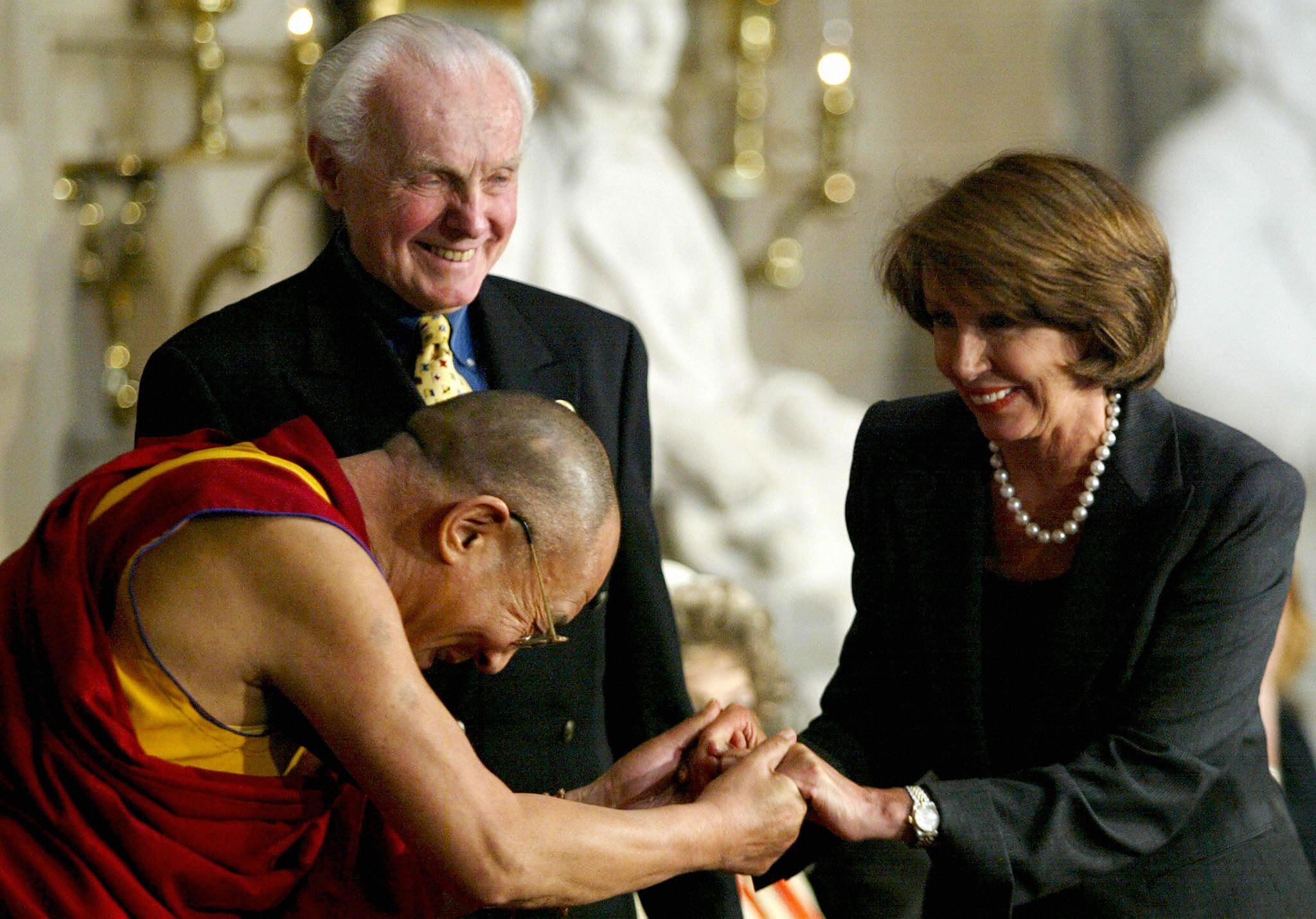 The Dalai Lama clasps hands with Nancy Pelosi while Tom Lantos watches during a 2003 congressional event on human rights.