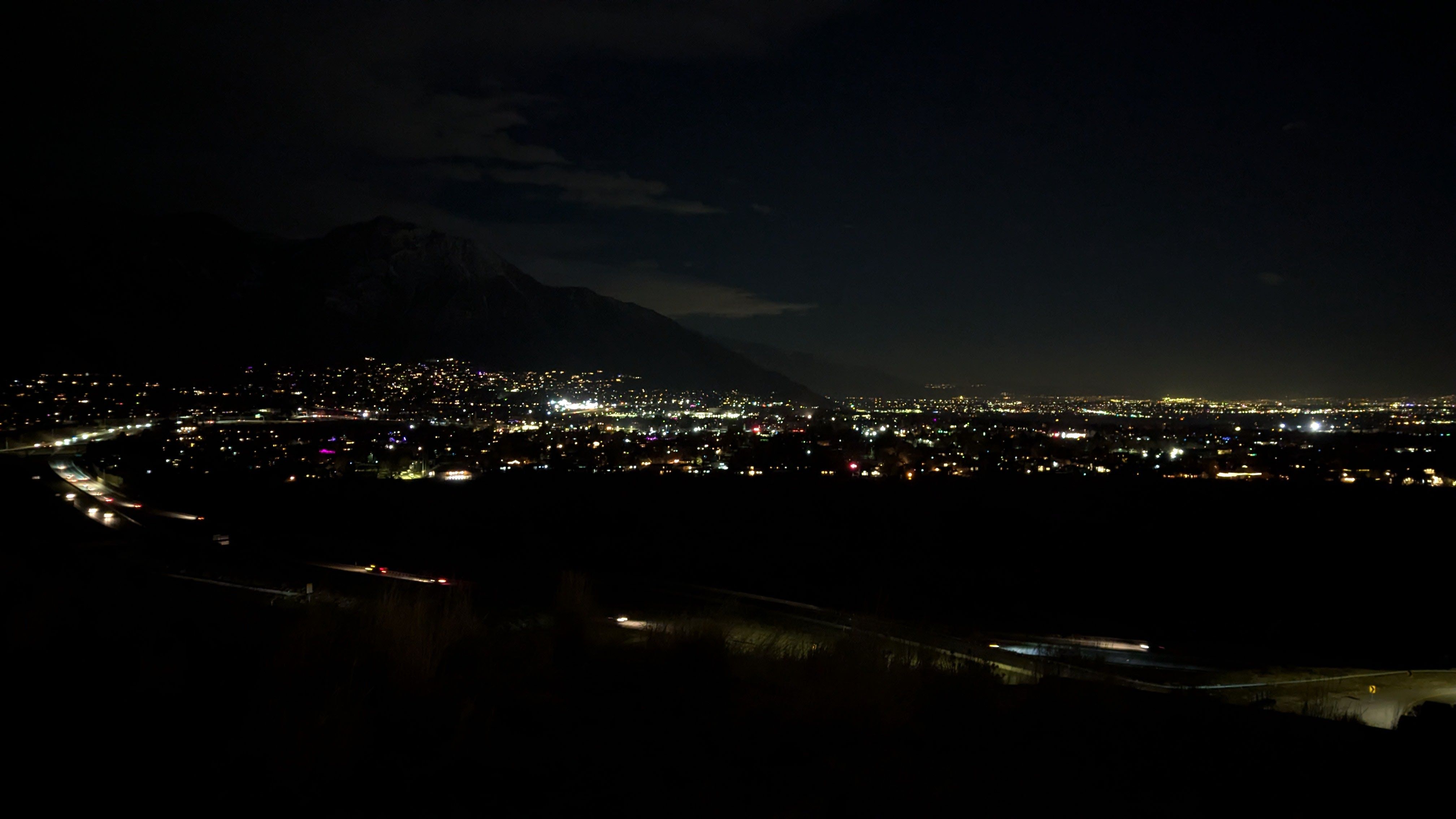 A city and highway at night from a nearby hill.