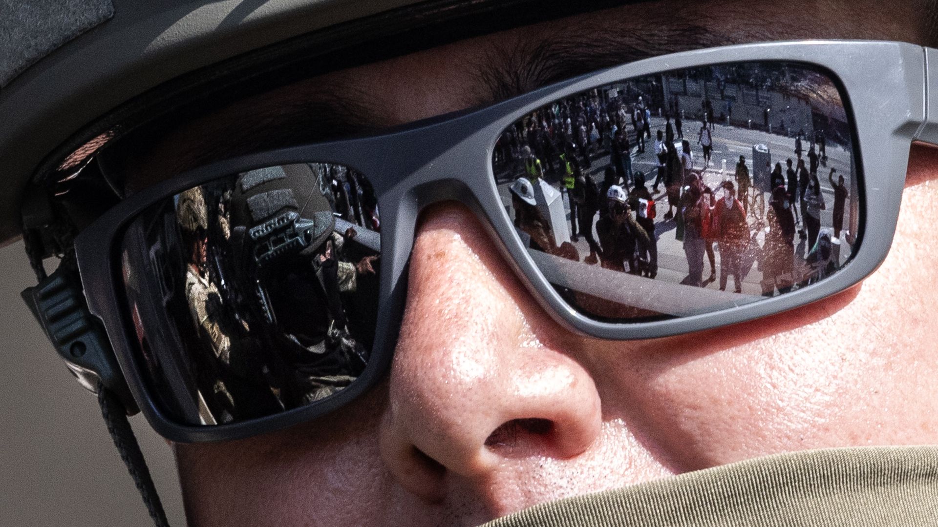 soldier with protesters reflected in his sunglasses