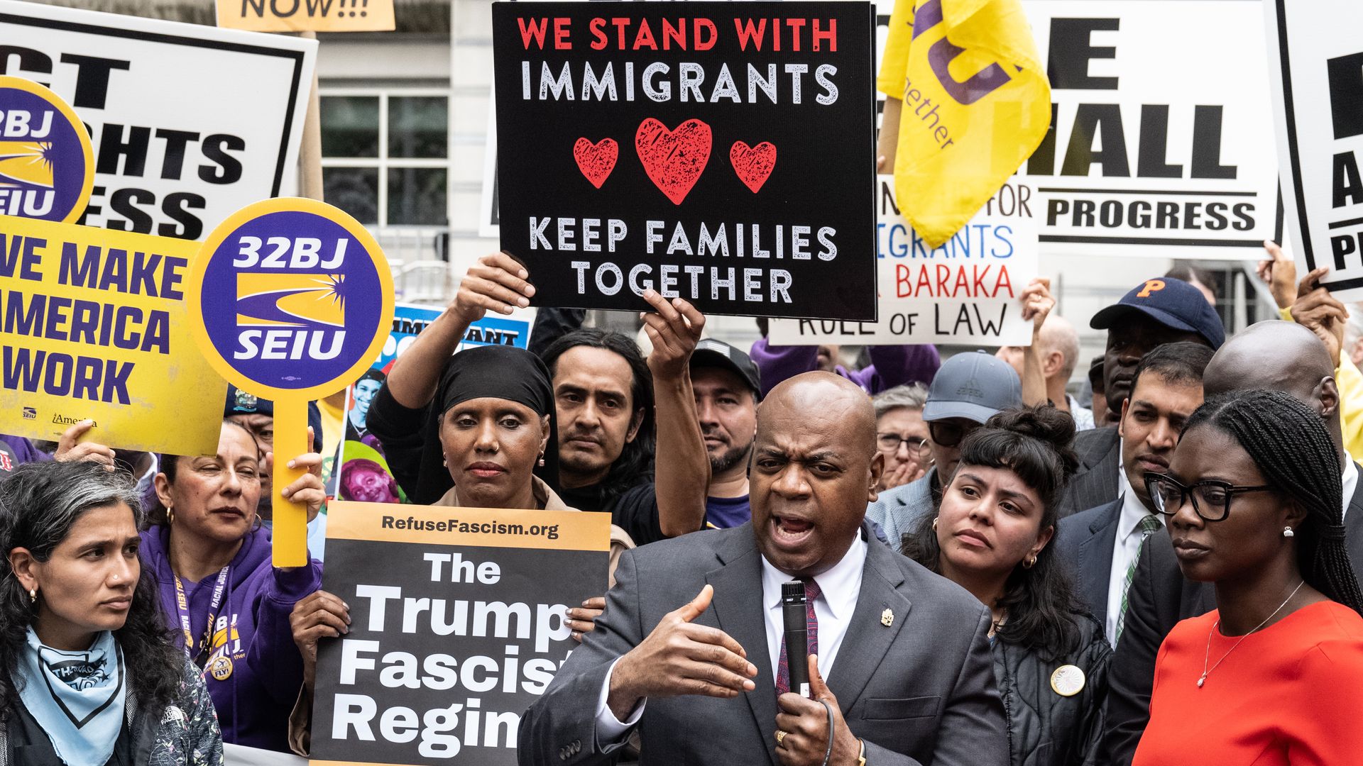 Baraka speaks into a microphone with a crowd of supporters holding signs 