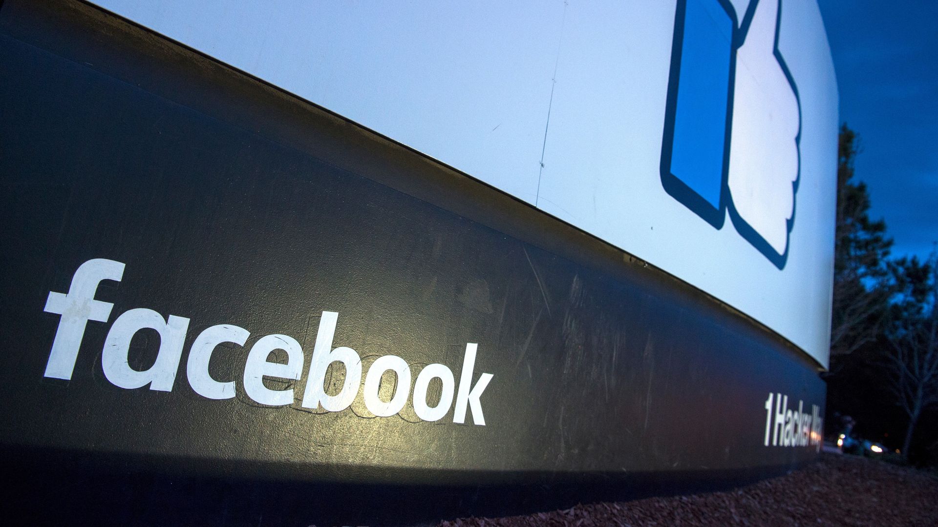 An angled-up photo of the "thumbs up" sign outside Facebook HQ at night