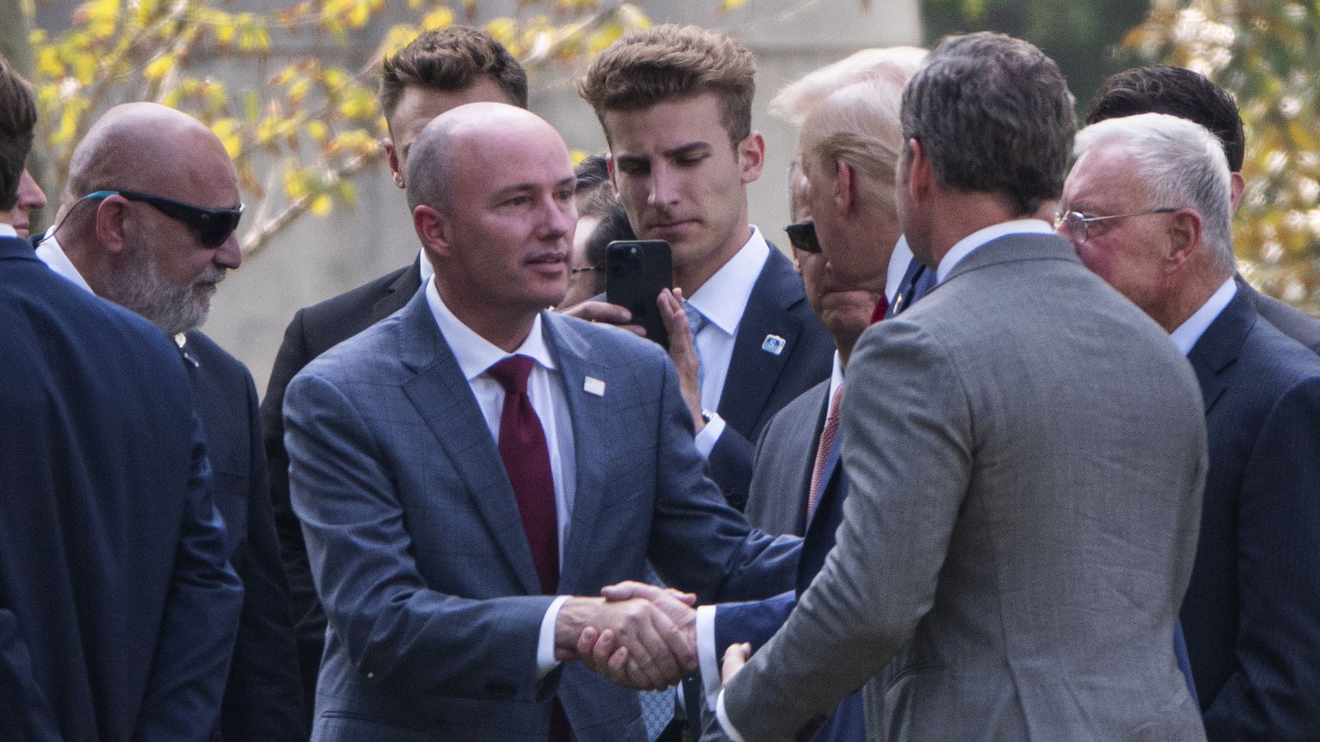 Utah Gov. Spencer Cox shakes hands with Trump at Arlington National Cemetery with a group of men in suits.