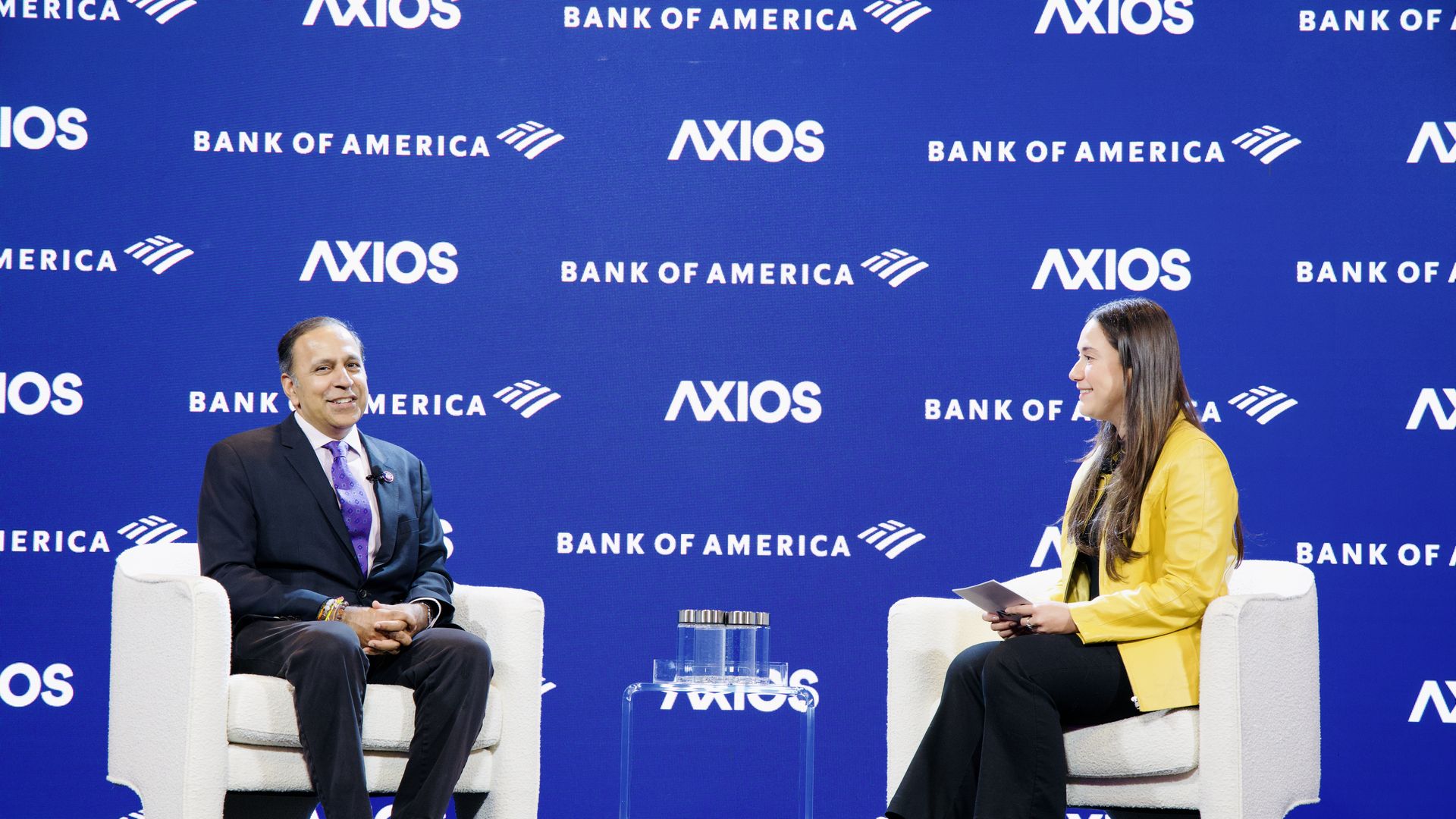Two people sitting in white chairs in front of a blue background with the words Axios and Bank of America