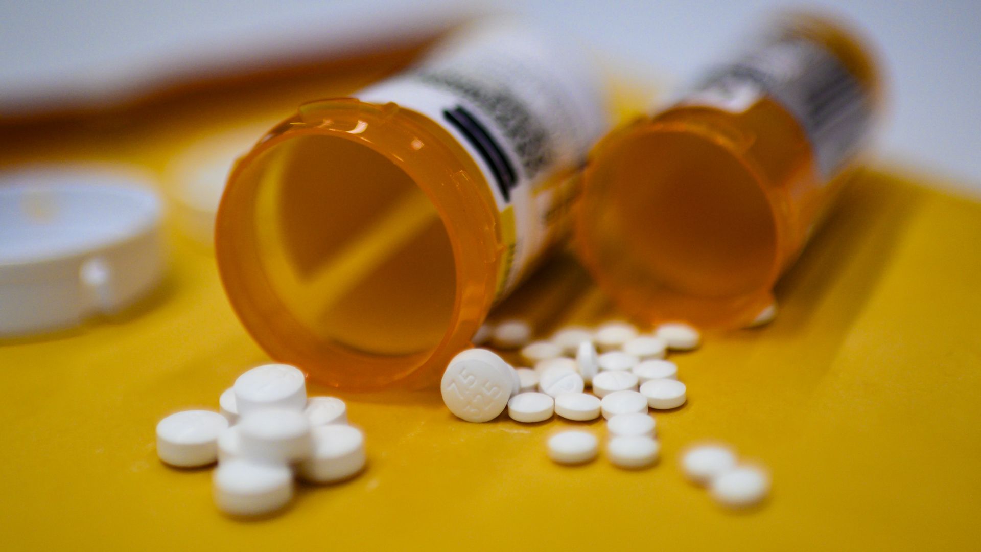 Two medication bottles with white oxycodone pills spilled nearby on a table.