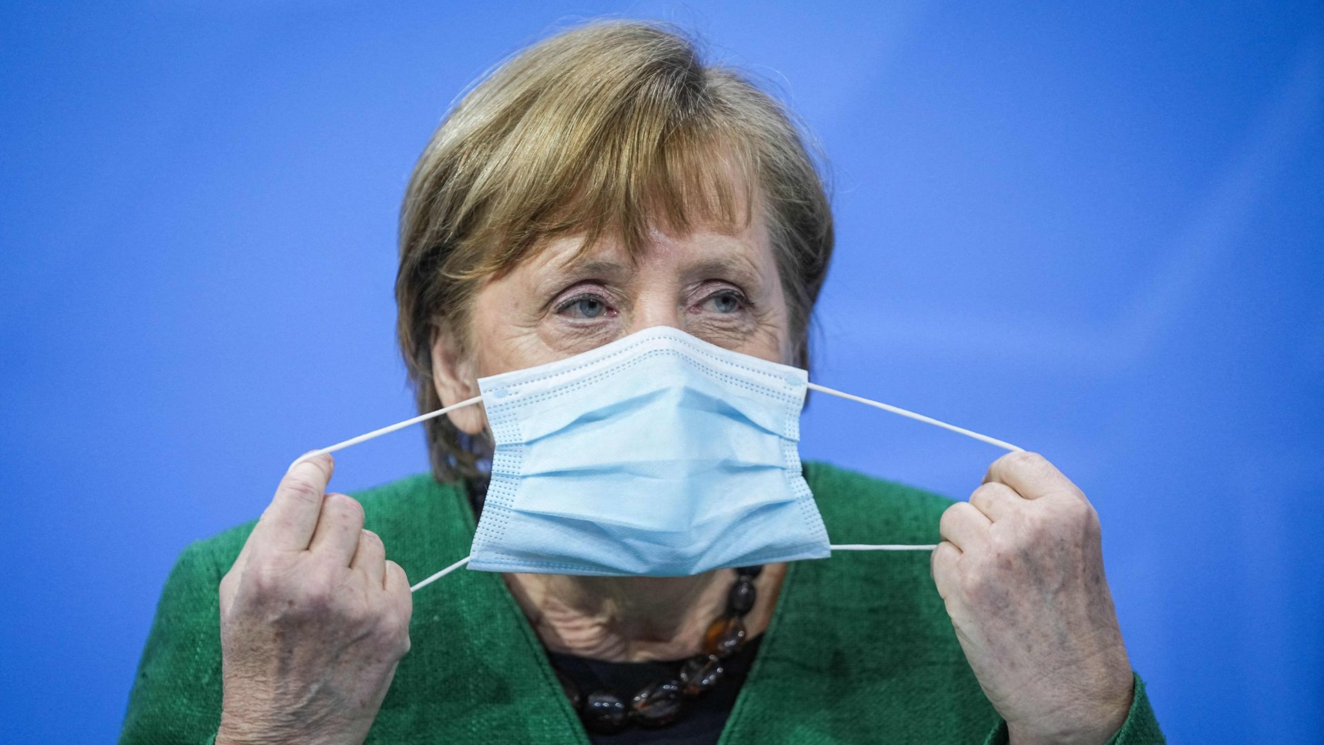 German Chancellor Angela Merkel removes her mask as she starts a press conference following talks via video conference with Germany's state premiers on the extension of the current lockdown March 22