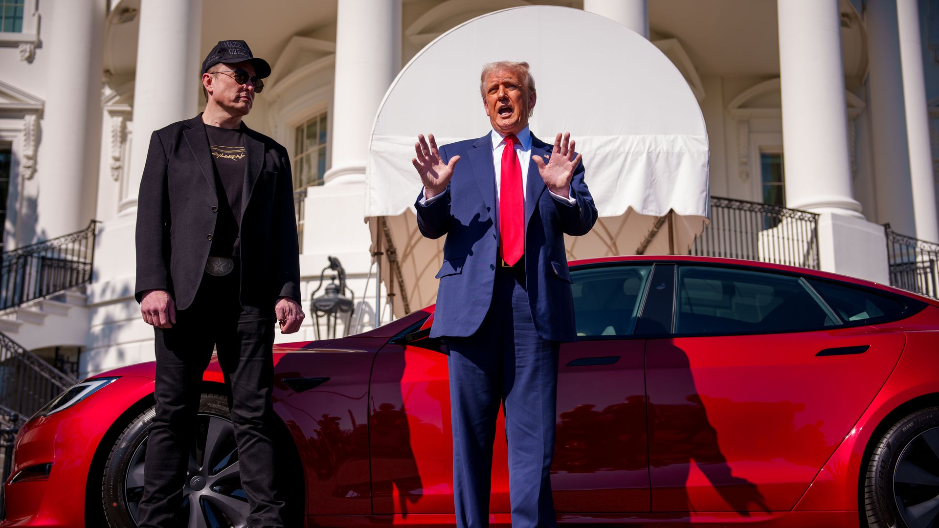 Elon Musk and Donald Trump stand in front of a red Tesla parked in front of the White House.