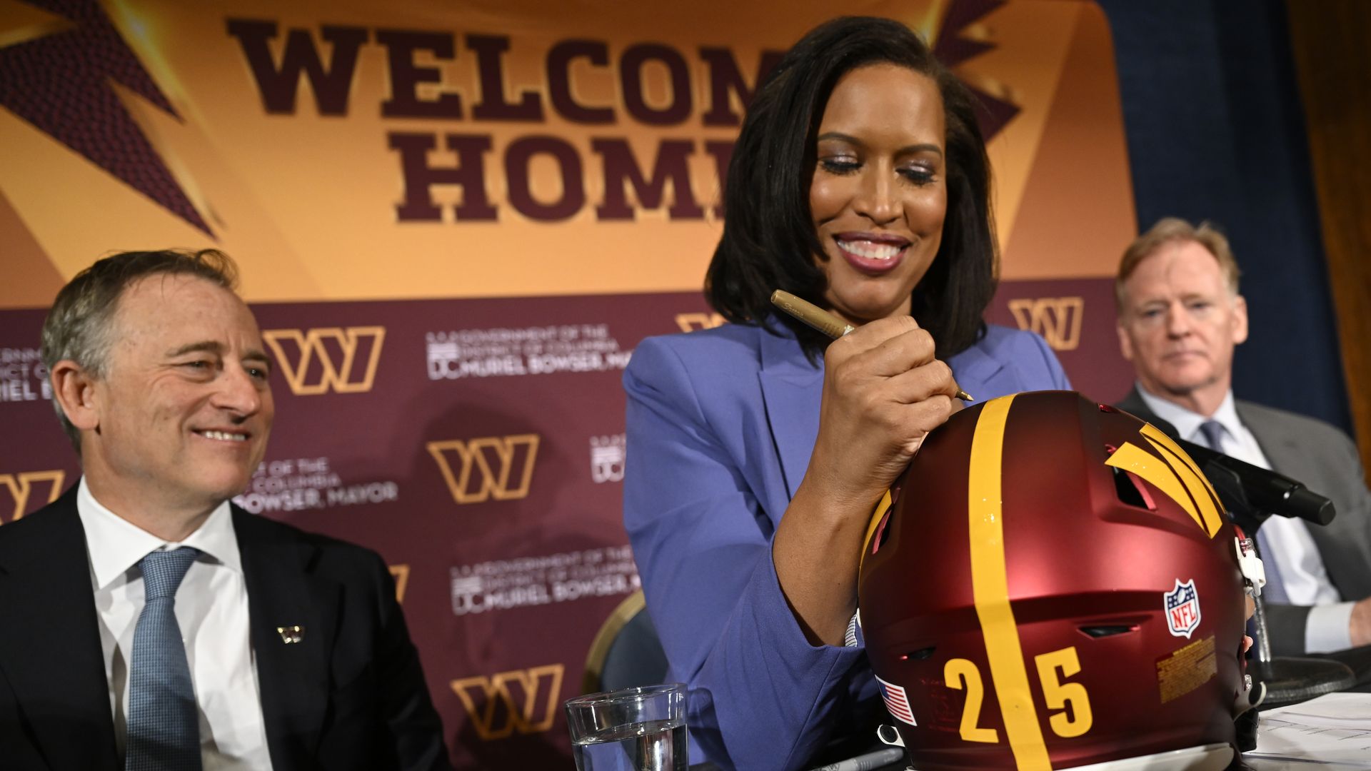 Mayor Muriel Bowser signs a Commanders helmet as NFL commissioner Roger Goodell and Commanders owner Josh Harris look on.