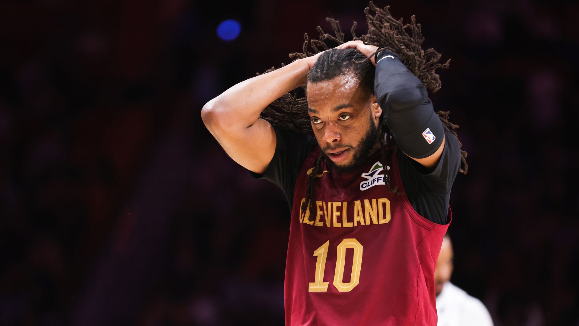 Cavs Darius Garland in a red jersey collecting his braids to tie. 