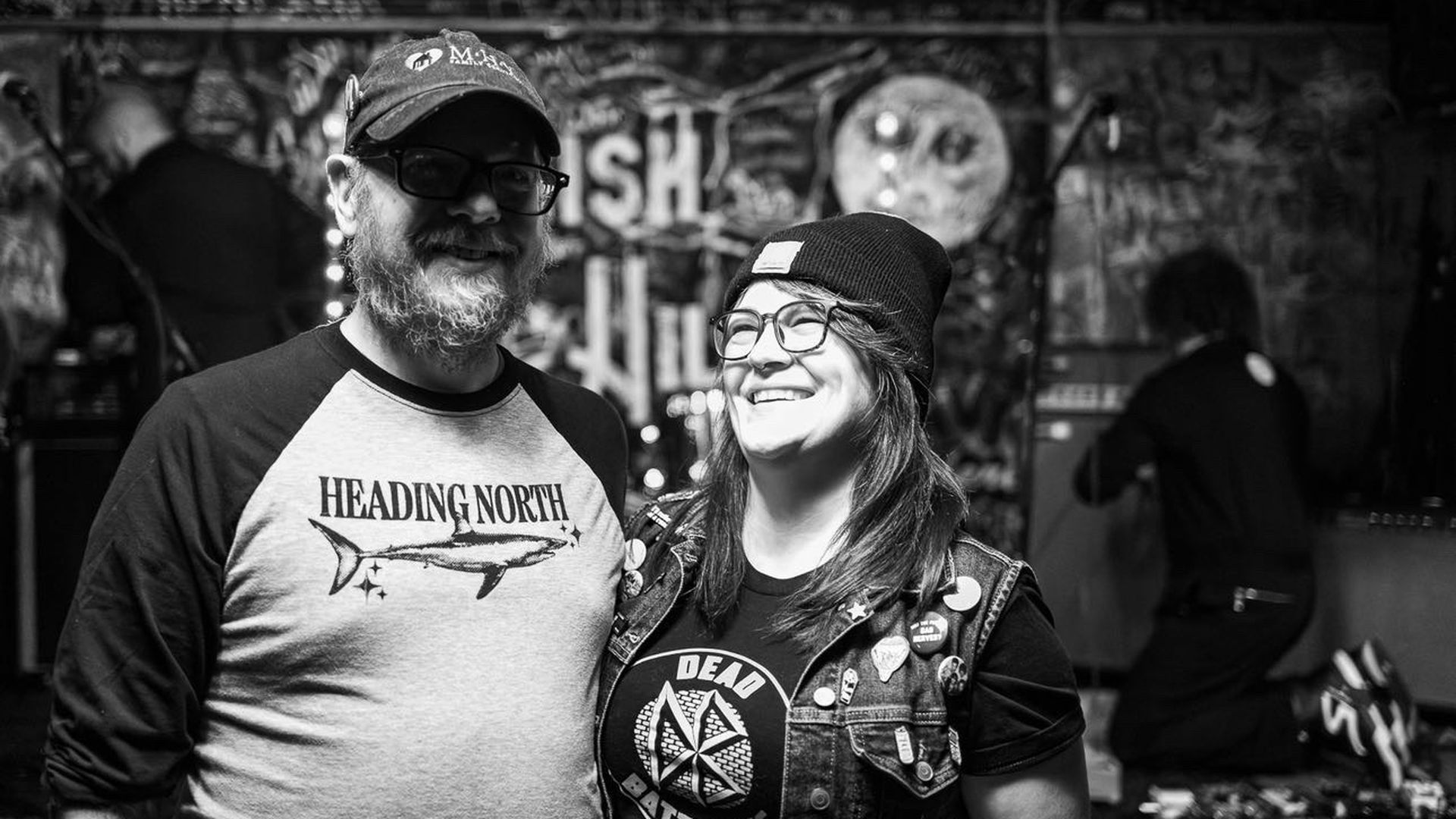 A couple in black and white stands at a concert venue. 