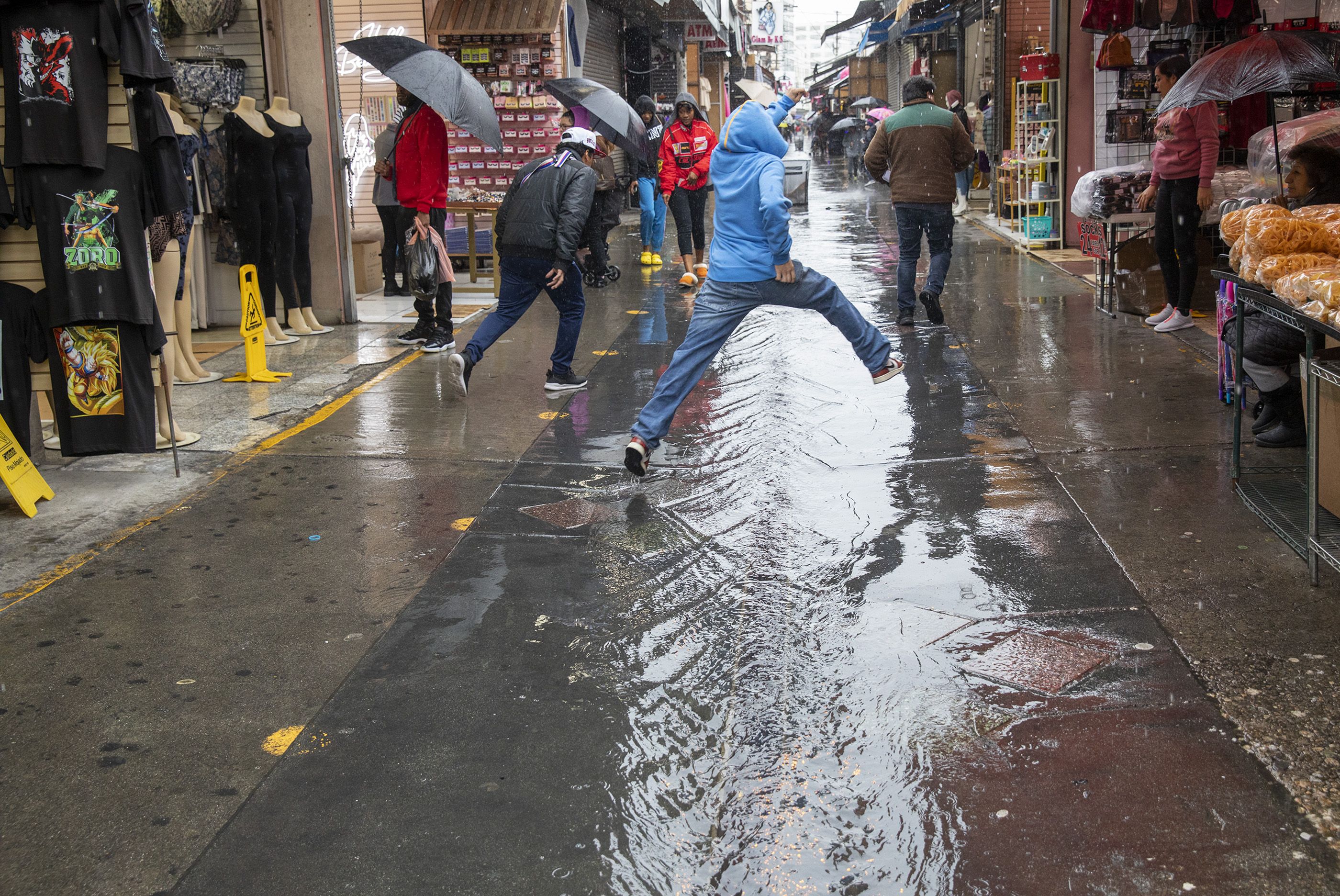 Brayan Suarez leaps to avoid getting wet while crossing to the other side as the rain water builds up on the ground at Santee Alley in Los Angeles. 