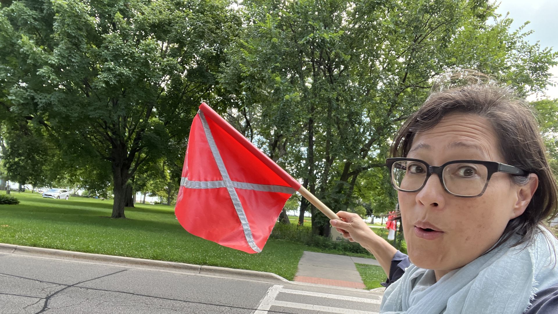 Monica Eng waving a small red flag at a cross walk on a street.