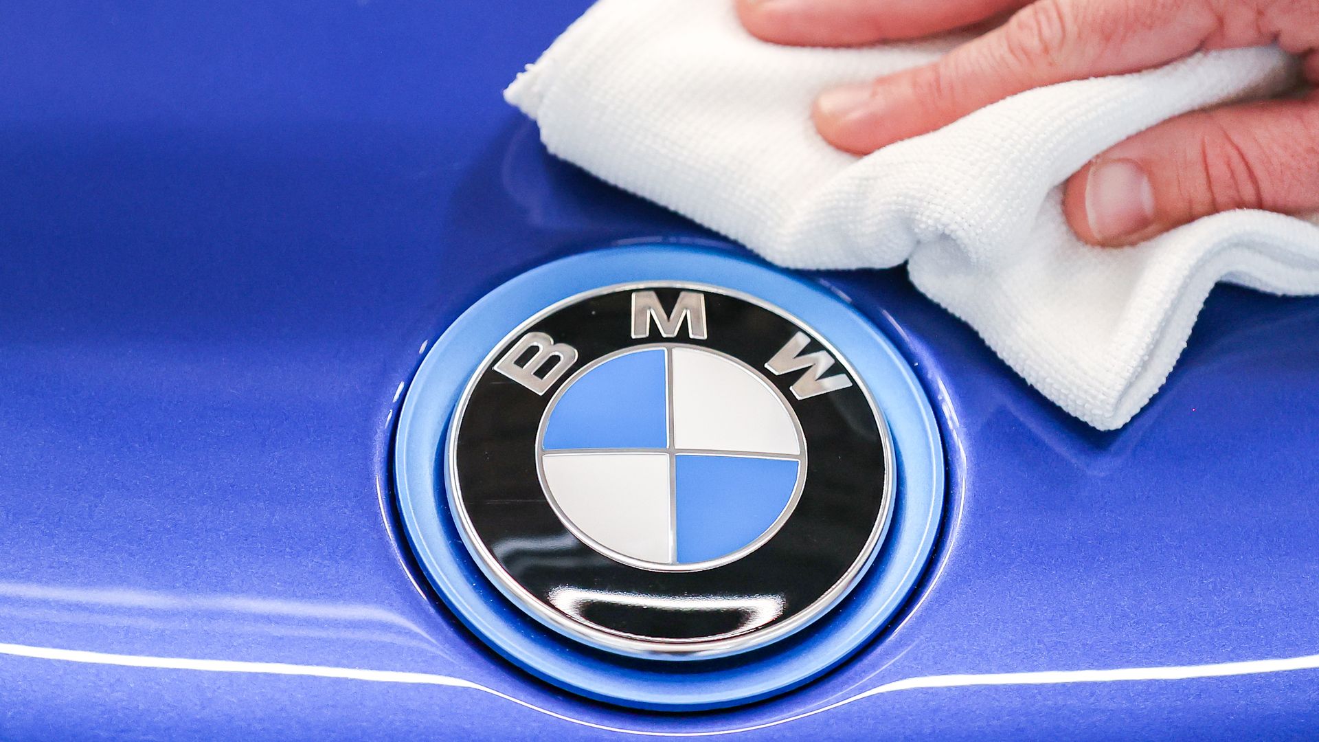 A hand wiping a car near the BMW logo with a white cloth