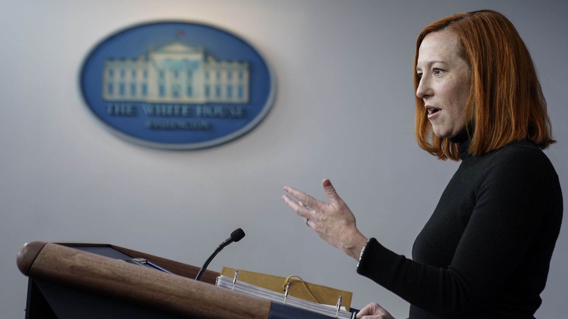 Jen Psaki stands at a podium with the White House logo in the background
