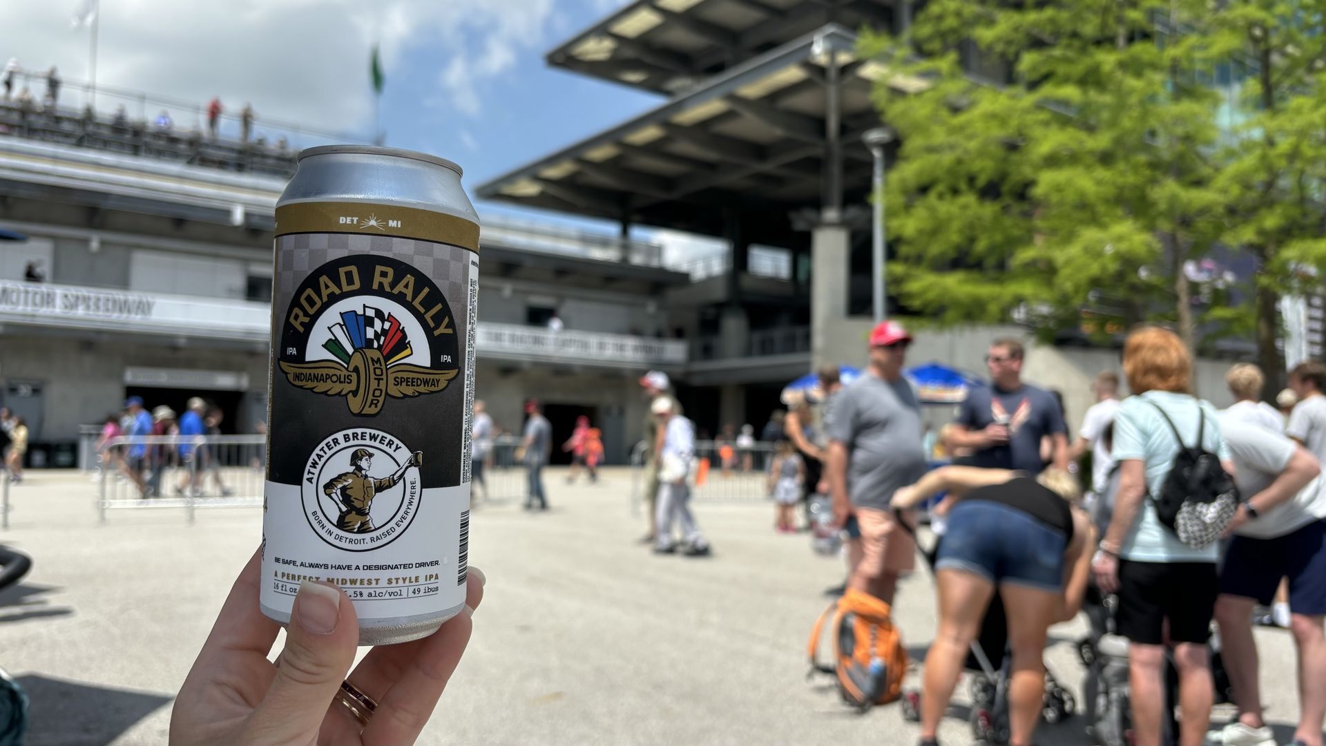 A hand holding a can of beer in front of the IMS pagoda
