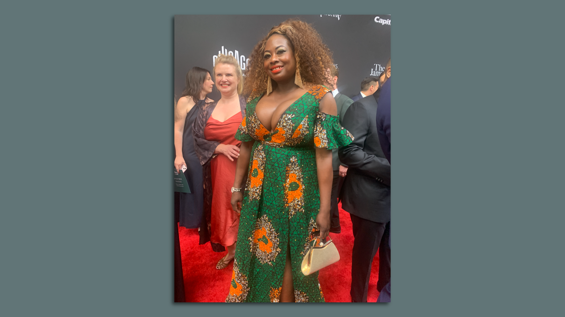 Tangie poses in a green and orange gown, with big gold earrings.