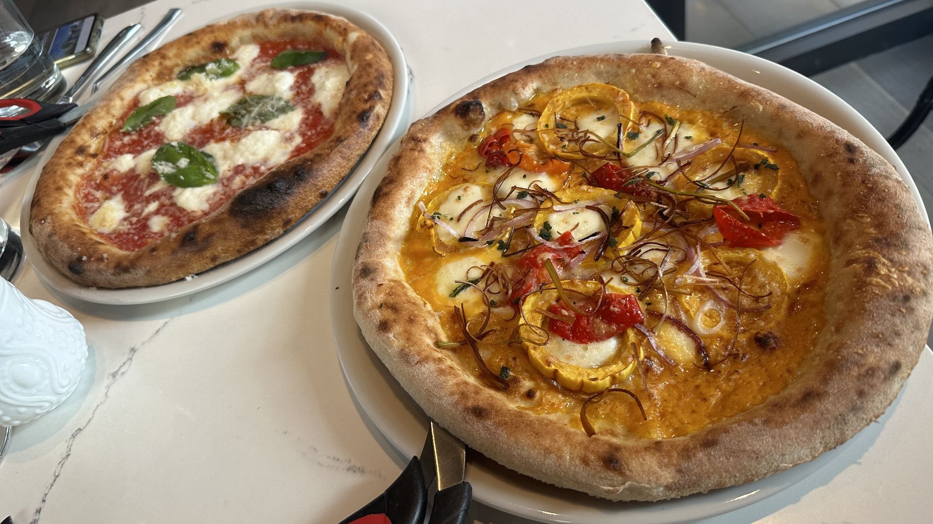 Two pizzas, one in the foreground with squash and orange butternut puree and one in the rear with bright red tomato sauce, basil and mozzerella.