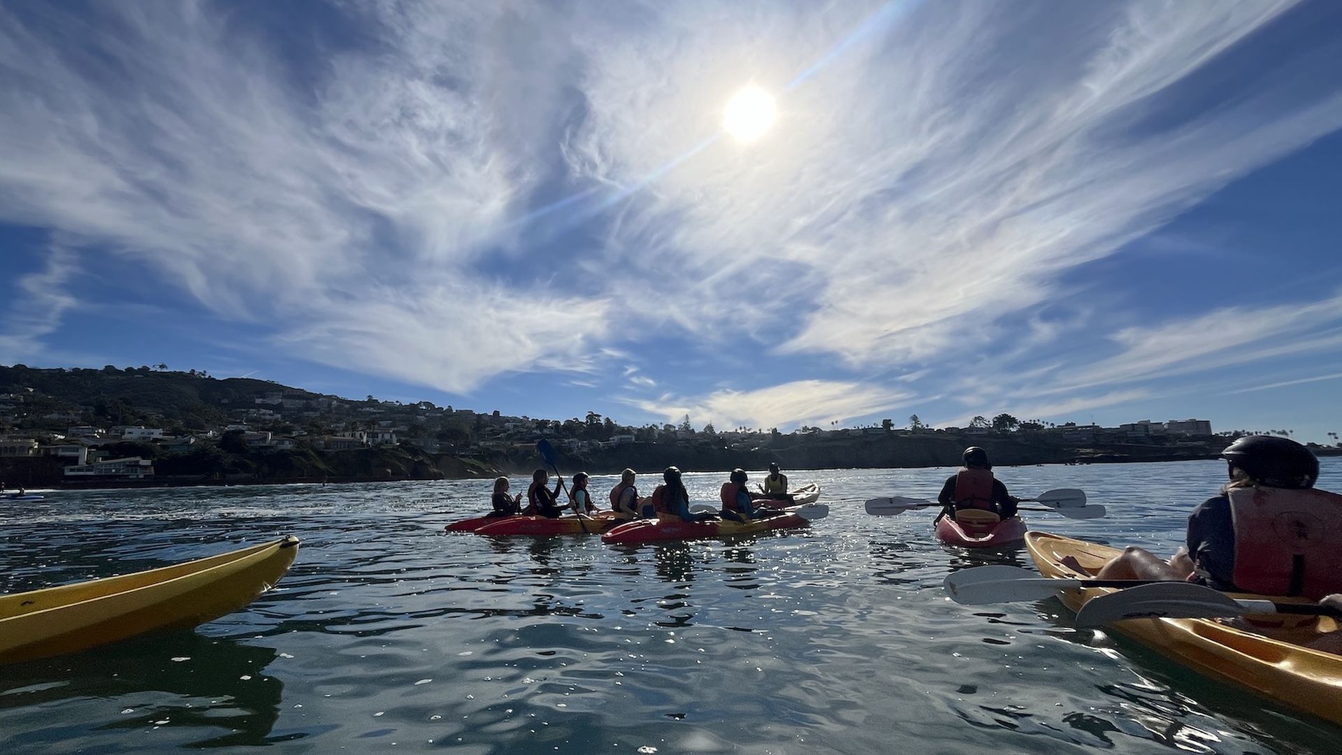 A group of kayakers in the ocean looking towards the coast on a sunny day. 