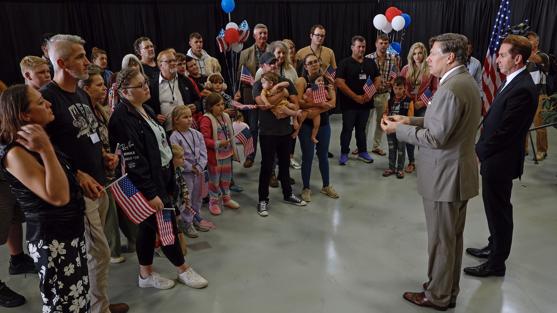 DULLES, VIRGINIA - MAY 12: Newly arrived South Africans listen to U.S. Deputy Secretary of State Christopher Landau and Homeland Security Deputy Secretary Troy Edgar (R) deliver welcome statements in a hangar at Atlantic Aviation Dulles near Washington Dulles International Airport on May 12, 2025 in