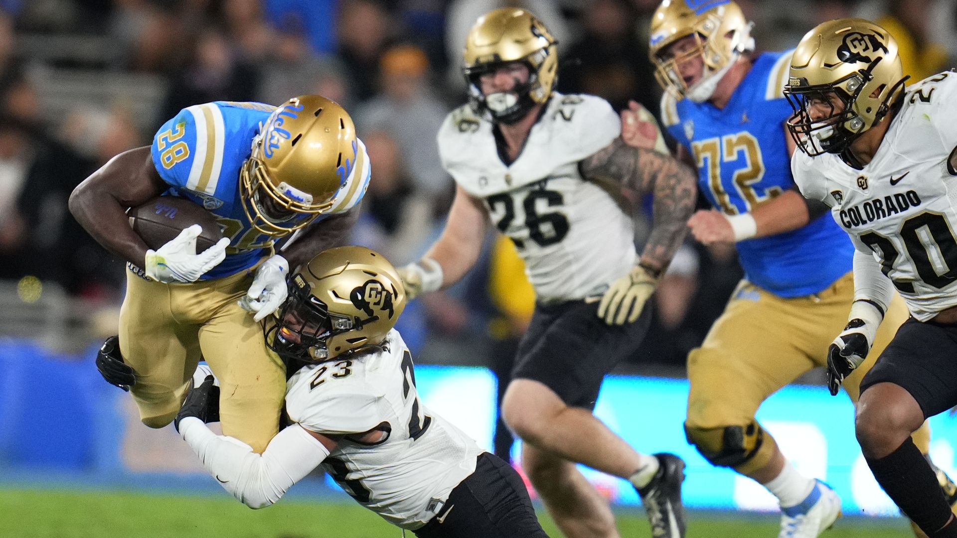 An American football player in a white jersey tackles a football player in a light-blue jersey during a nighttime college football game. 
