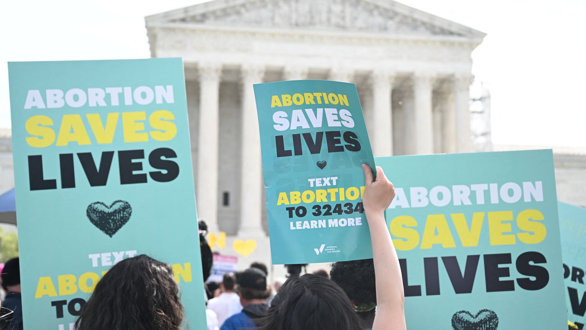 Protestors outside of the Supreme Court hold posters that say "abortion saves lives." 
