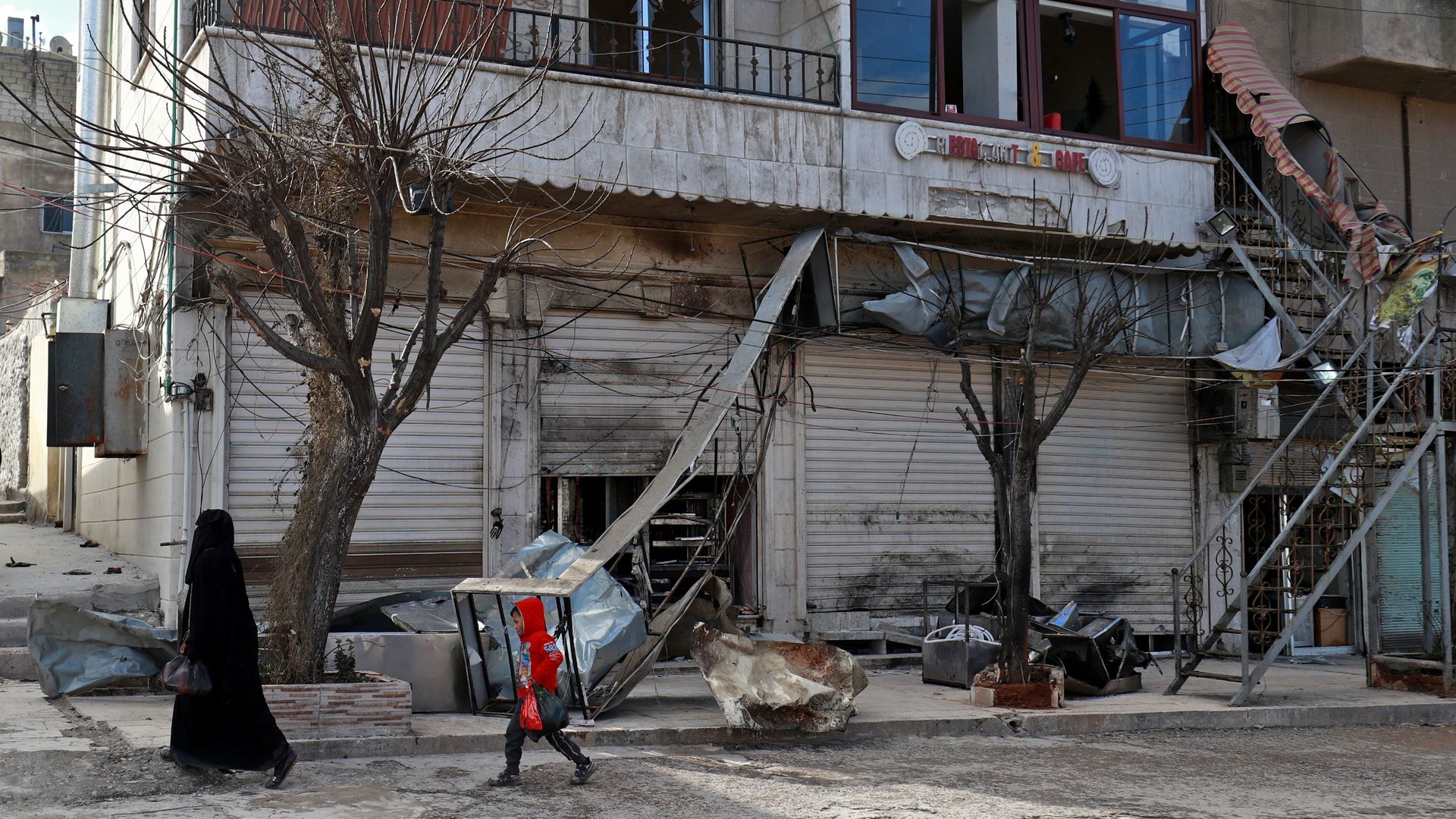 A Syrian woman and child walk past the shuttered doors of a restaurant which was the site of a suicide attack in northern Syria which killed four US servicemen.