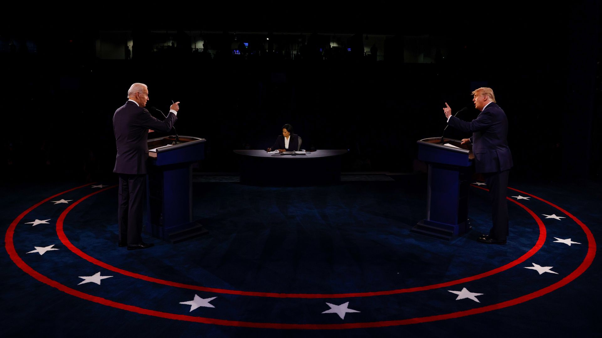 Biden, left, and Trump, right, on a debate stage in 2020. They stand in a circle that has stars on it and both are pointing. The photo is taken from behind.