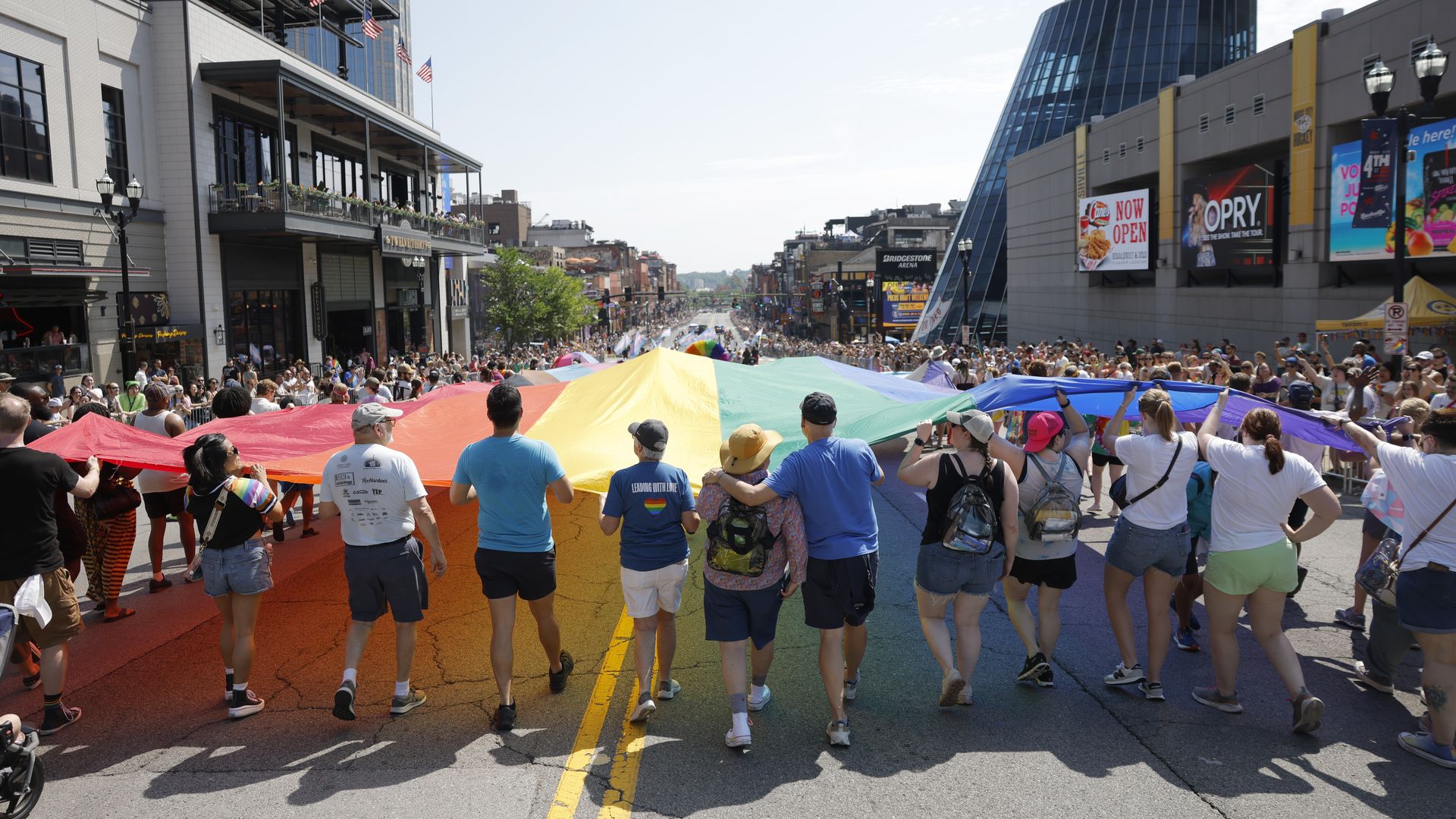 A crowd of people hold up a large rainbow flag in a pride parade.