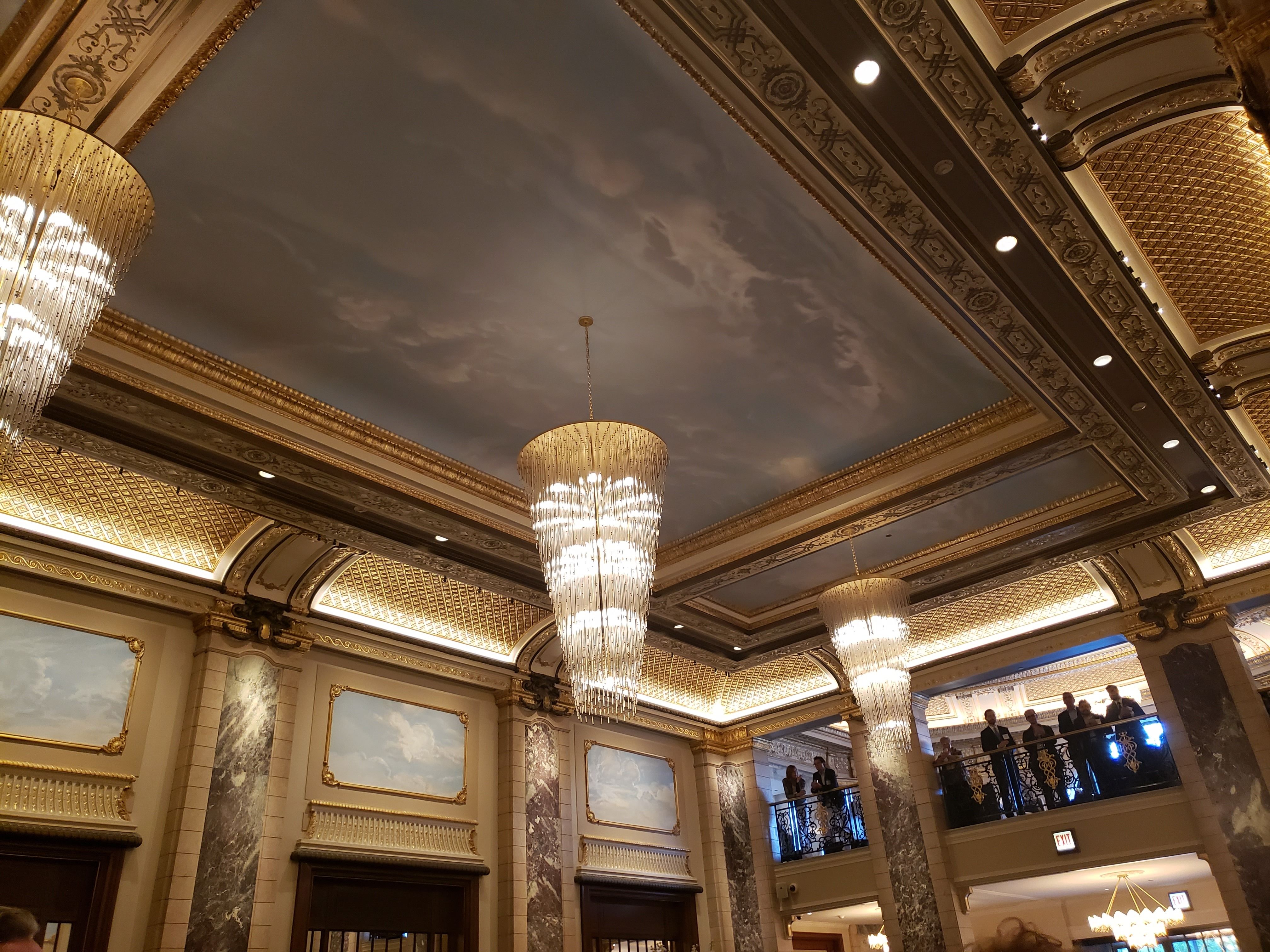 The gold gilded ceiling of the Belden-Stratford, with three large cascading chandeliers hanging.