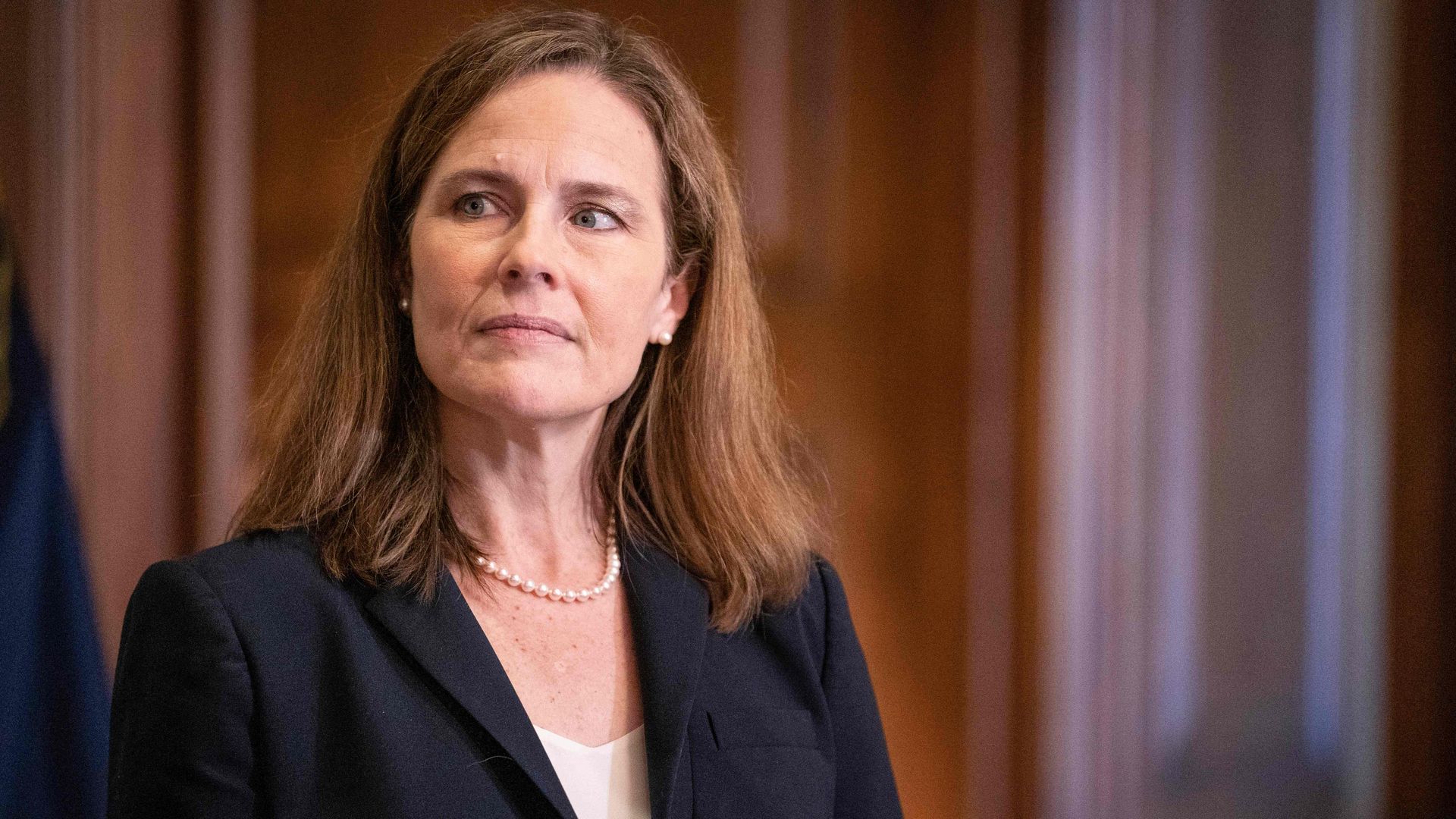 Amy Coney Barrett looks to her right while wearing a black blazer and pearls