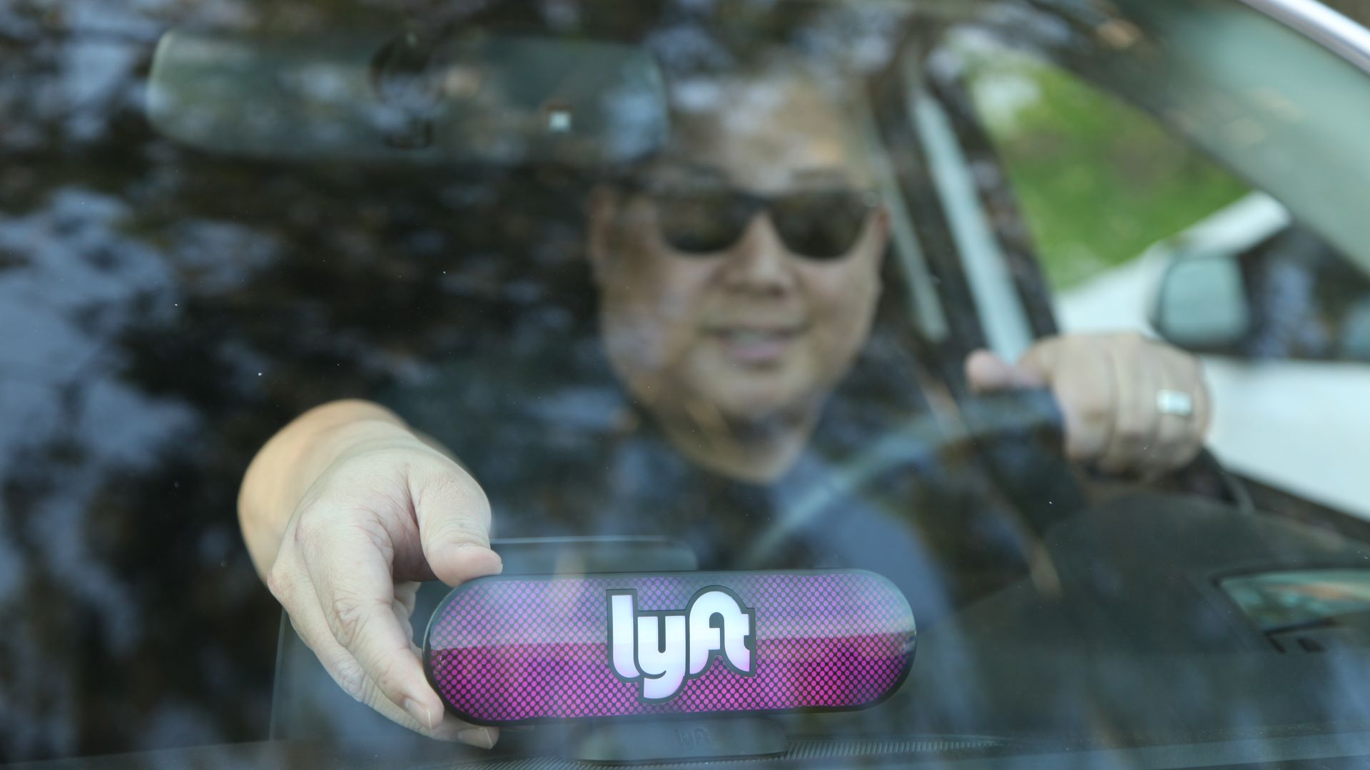 Driver behind the wheel with an illuminated Lyft sign on dashboard
